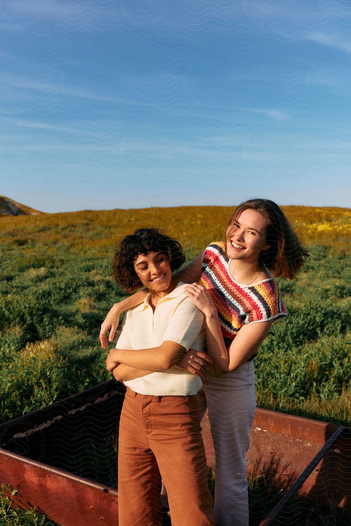 two females smiling while posing near a grass field in daytime