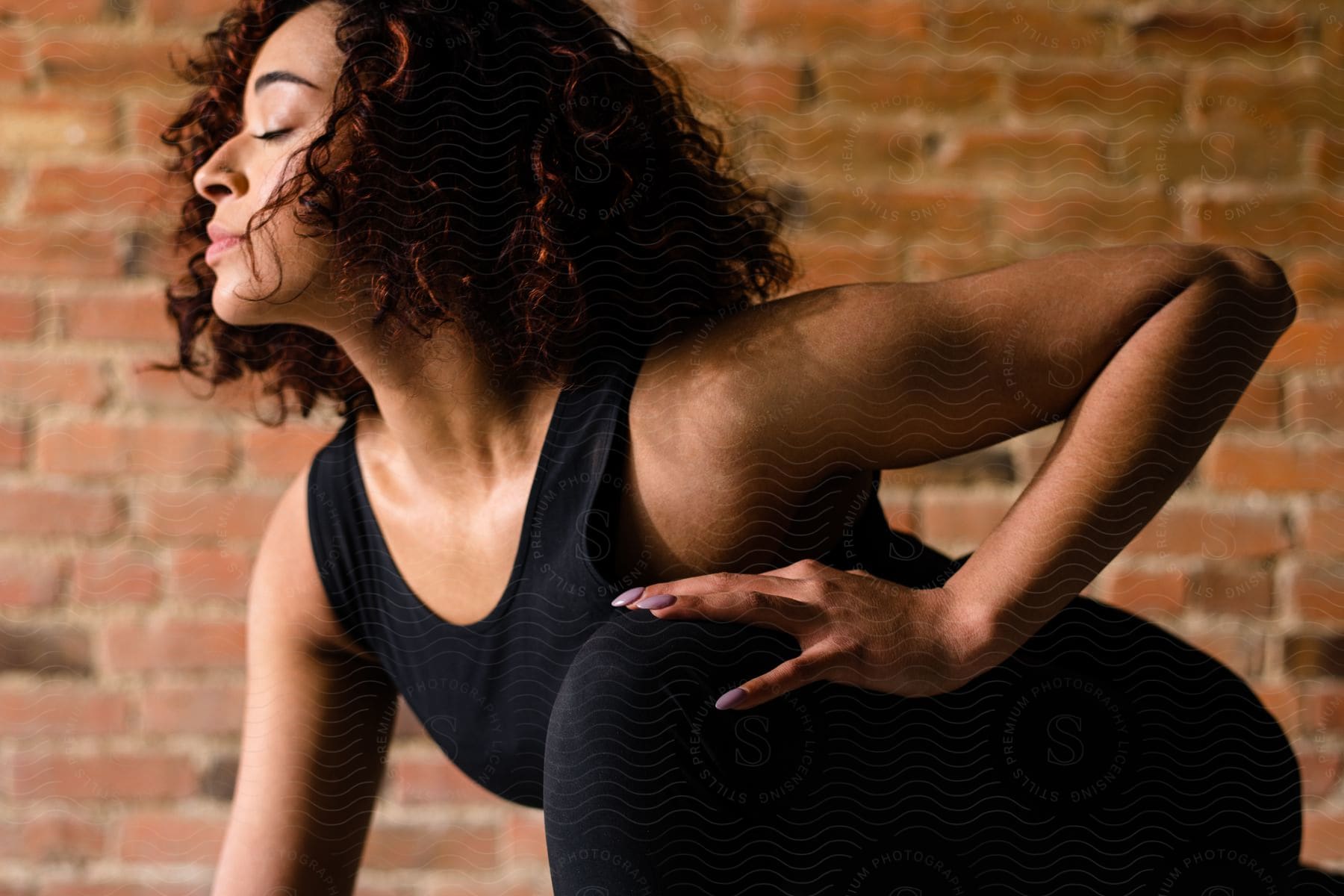 A young black woman is bending toward the floor while stretching her leg and thigh.