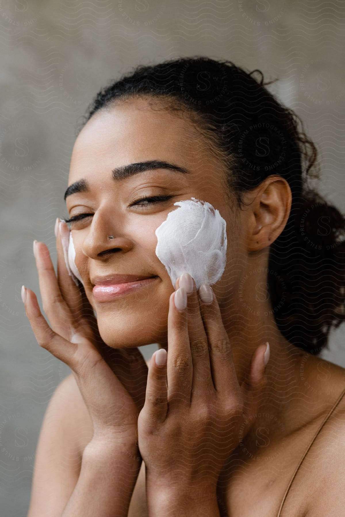 A woman is applying a white lotion to her cheeks.