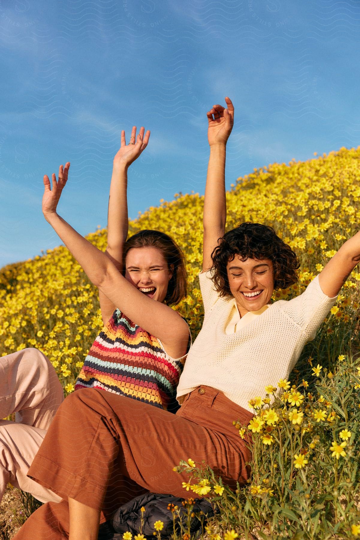 Two women traveling out in a field of flowers having fun.