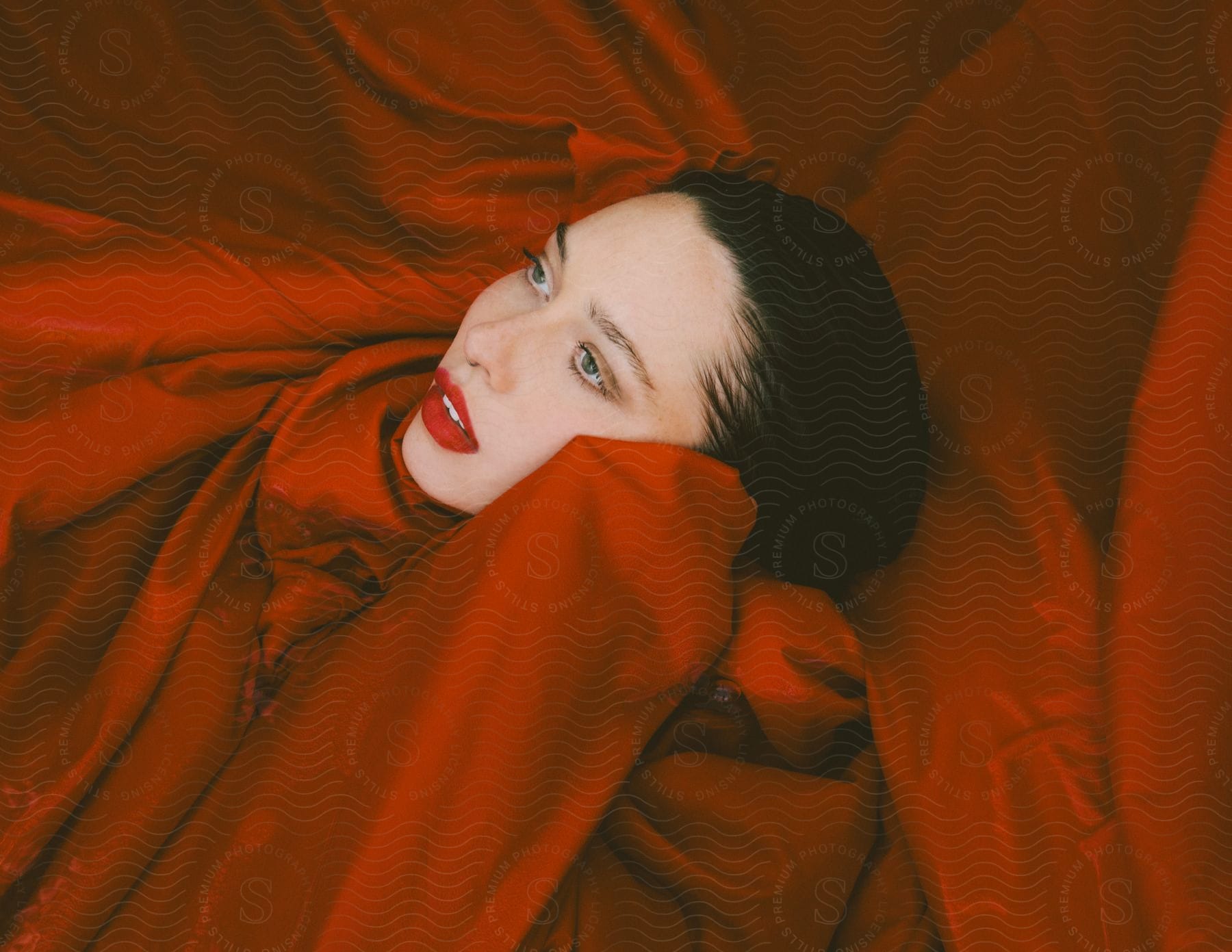 With her face turned upwards, a woman is enveloped in red cloth.