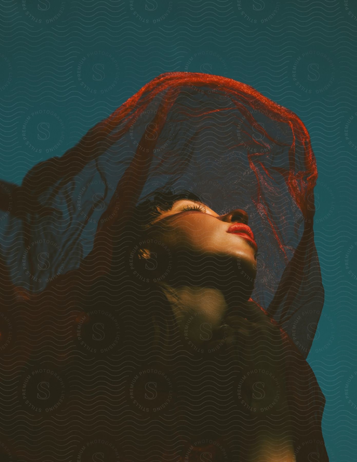 a woman poses with a sheer red scarf over her head