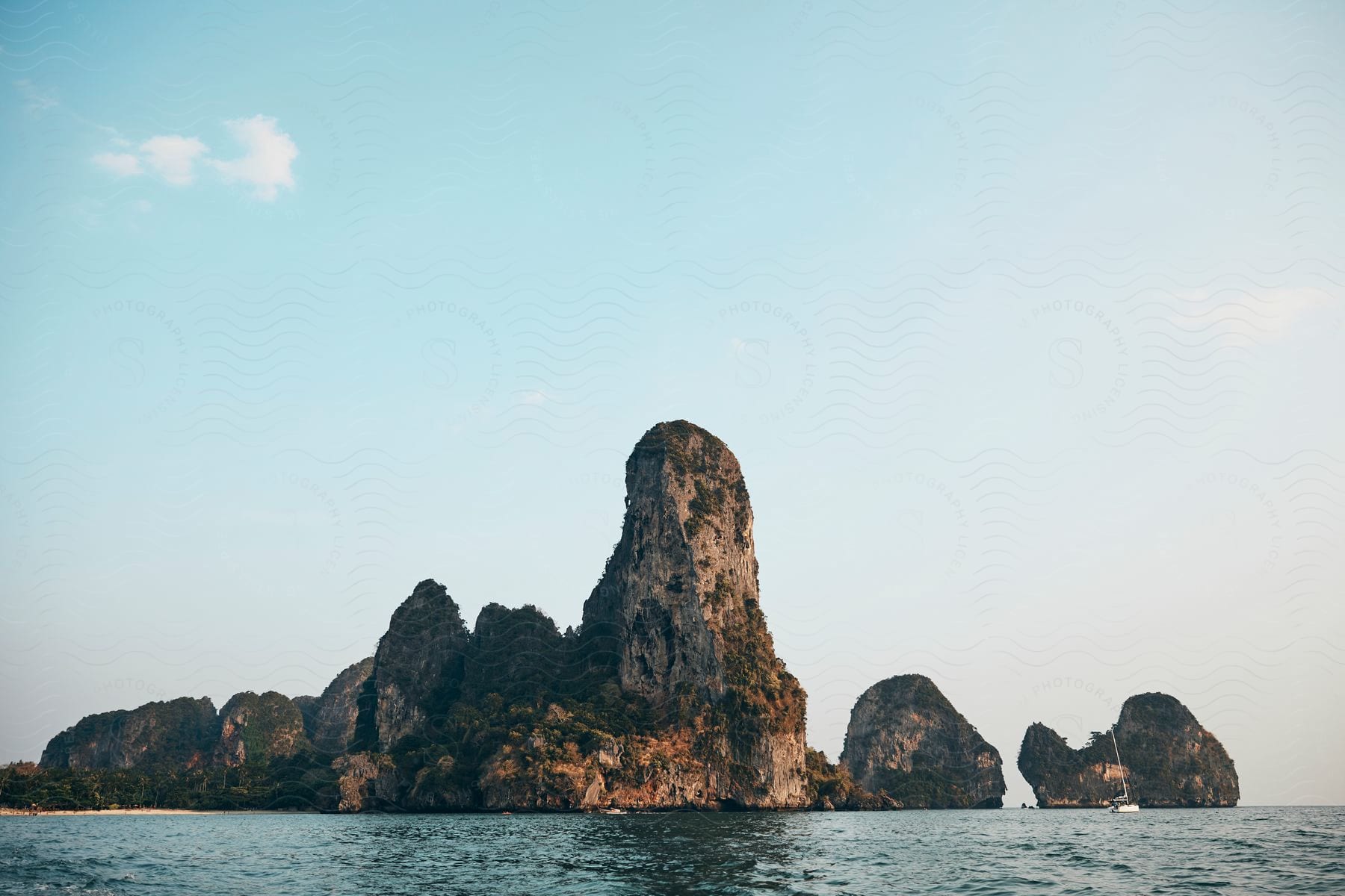 Green And Brown Rocky Formation In The Sea Under White Clouds And A Blue Sky During The Day