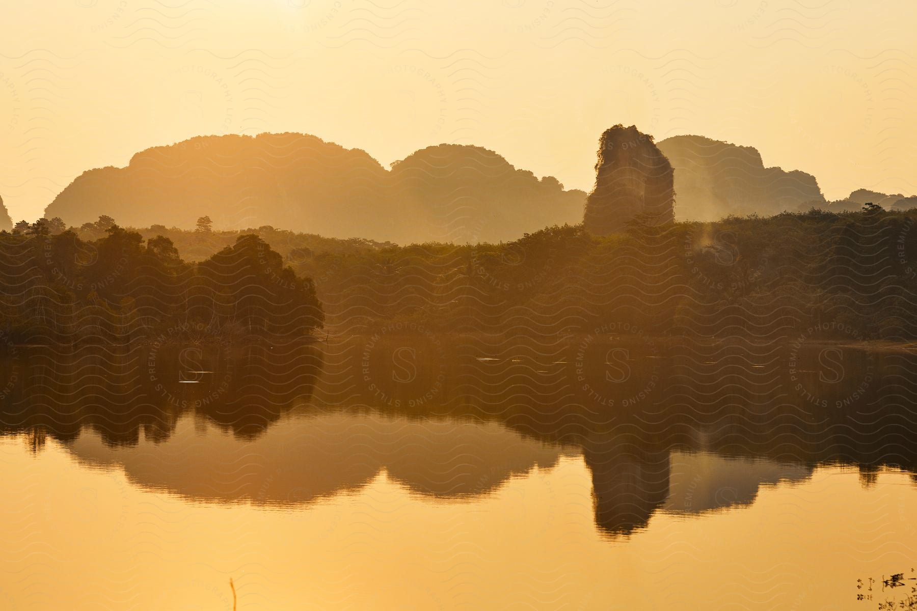 Landscape of A body of water with A reflection of a mountain and large rock formation with trees.