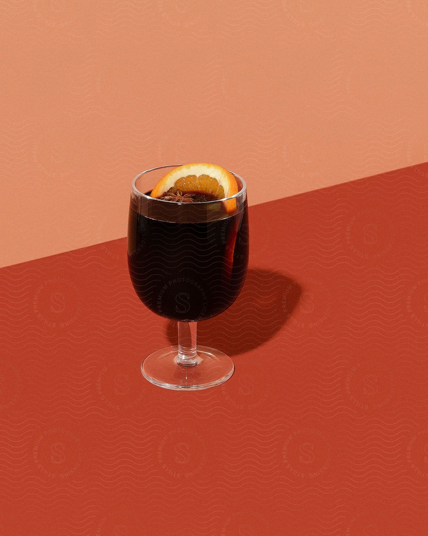 A glass has a serving of a beverage with a slice of orange as a garnish.