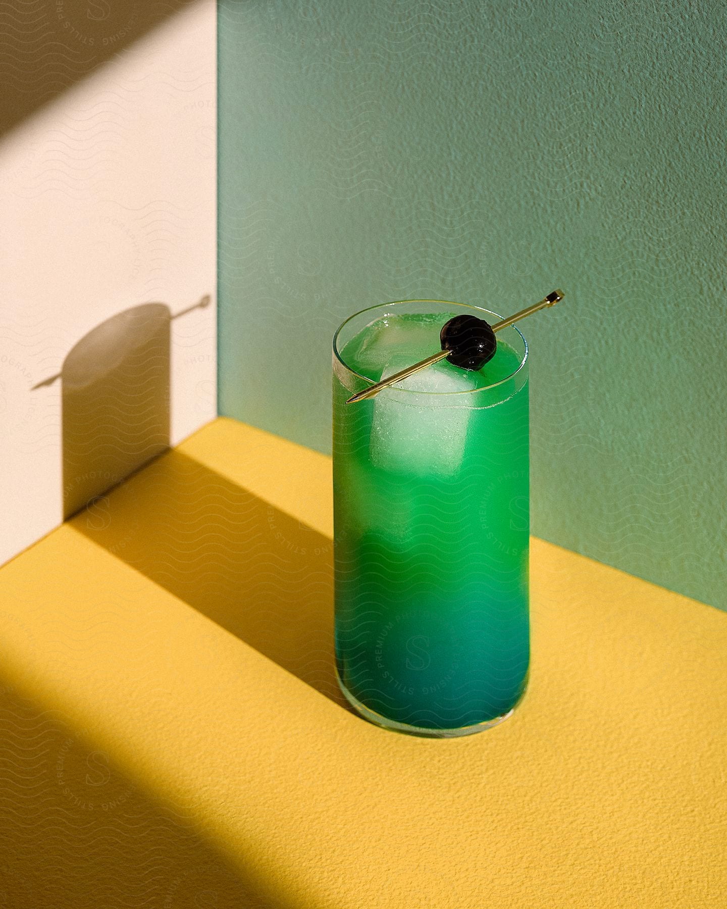 iced green beverage served with olive garnish over a yellow table next to a green wall