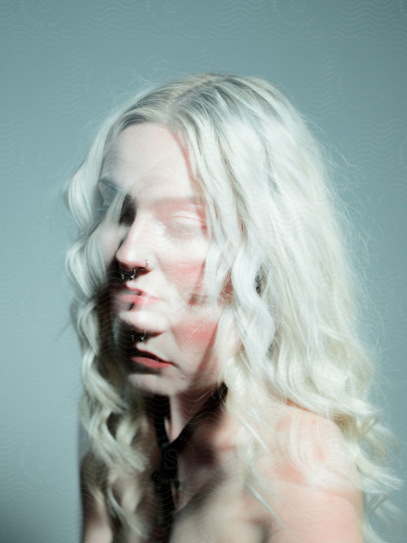 A woman with shoulder-length curly white hair poses for a multi-exposure portrait, a black tie around her neck.