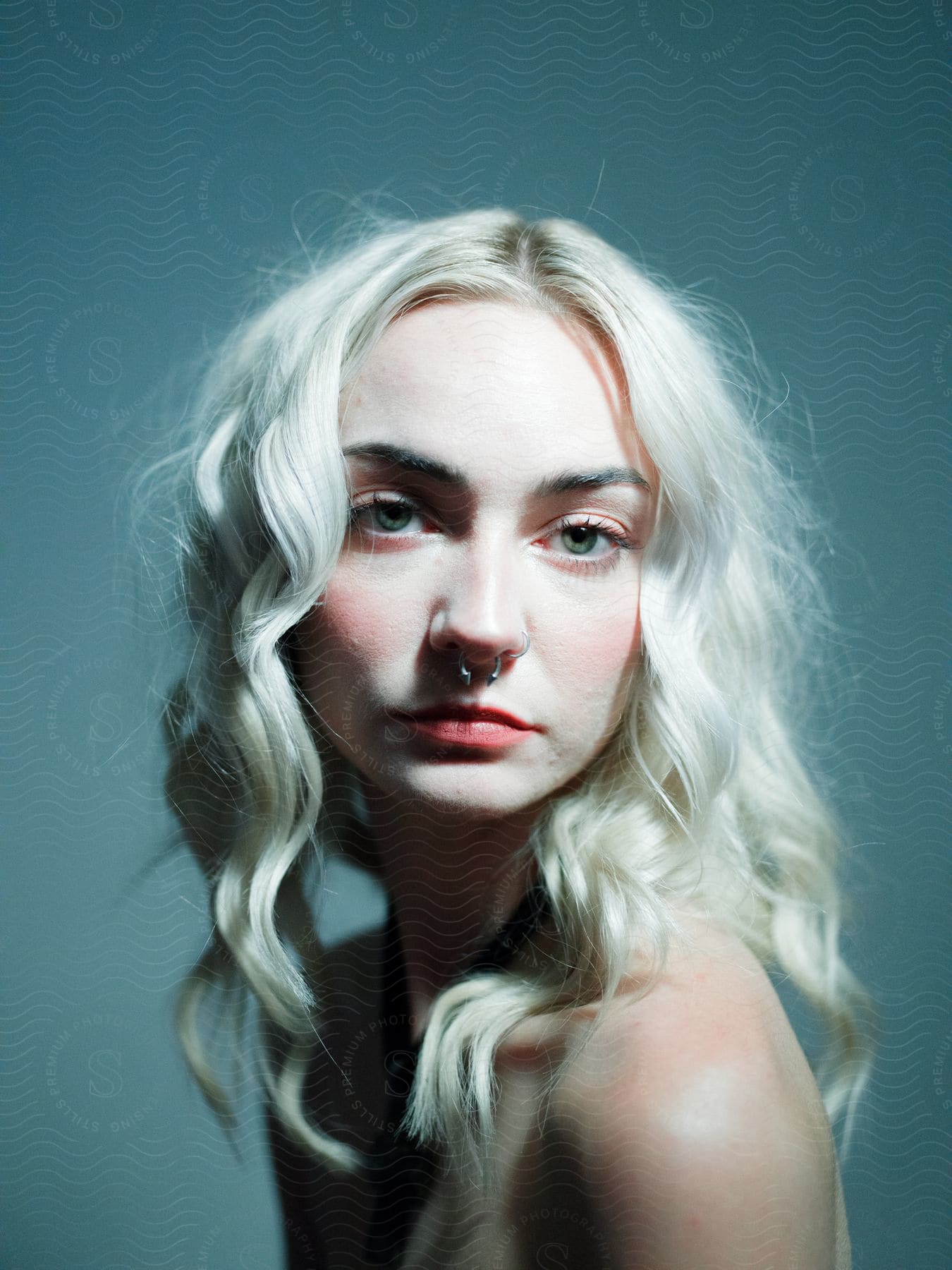 A woman with long wavy blonde hair and wearing a nose ring is looking ahead