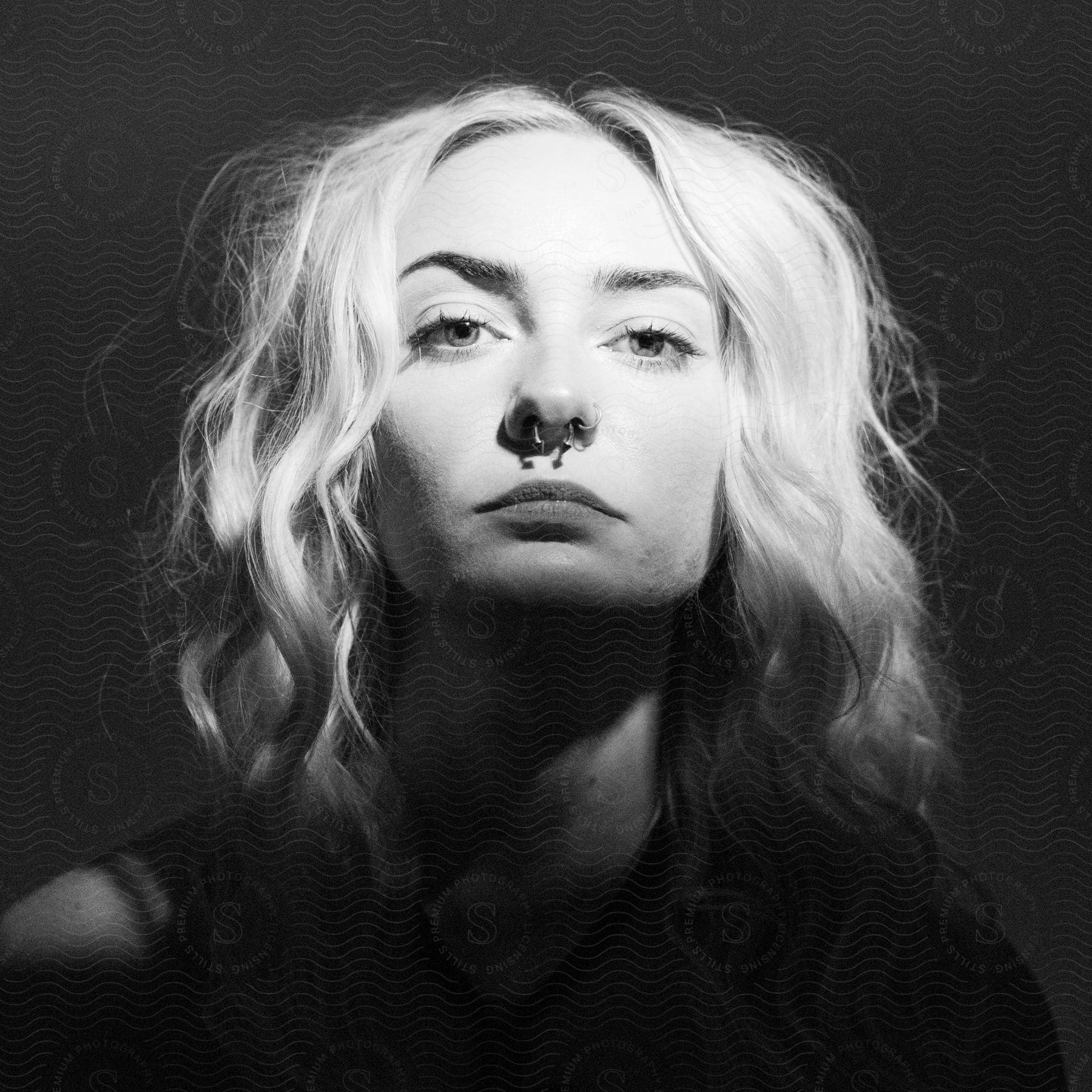 a woman with a nose piercing stands under a light in a dim room