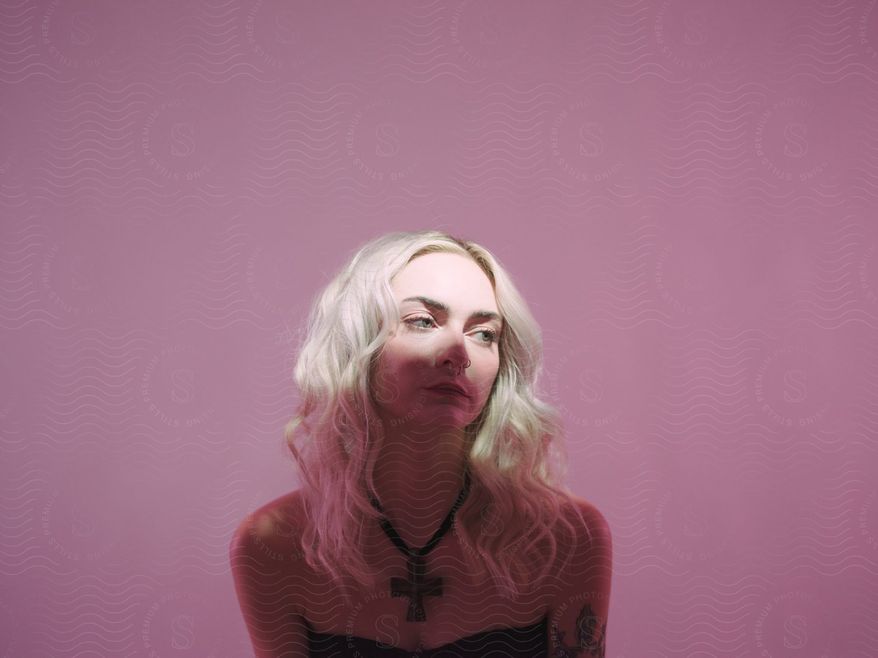 blonde woman with a cross necklace and a contemplative face expression posing indoors next to a purple wall