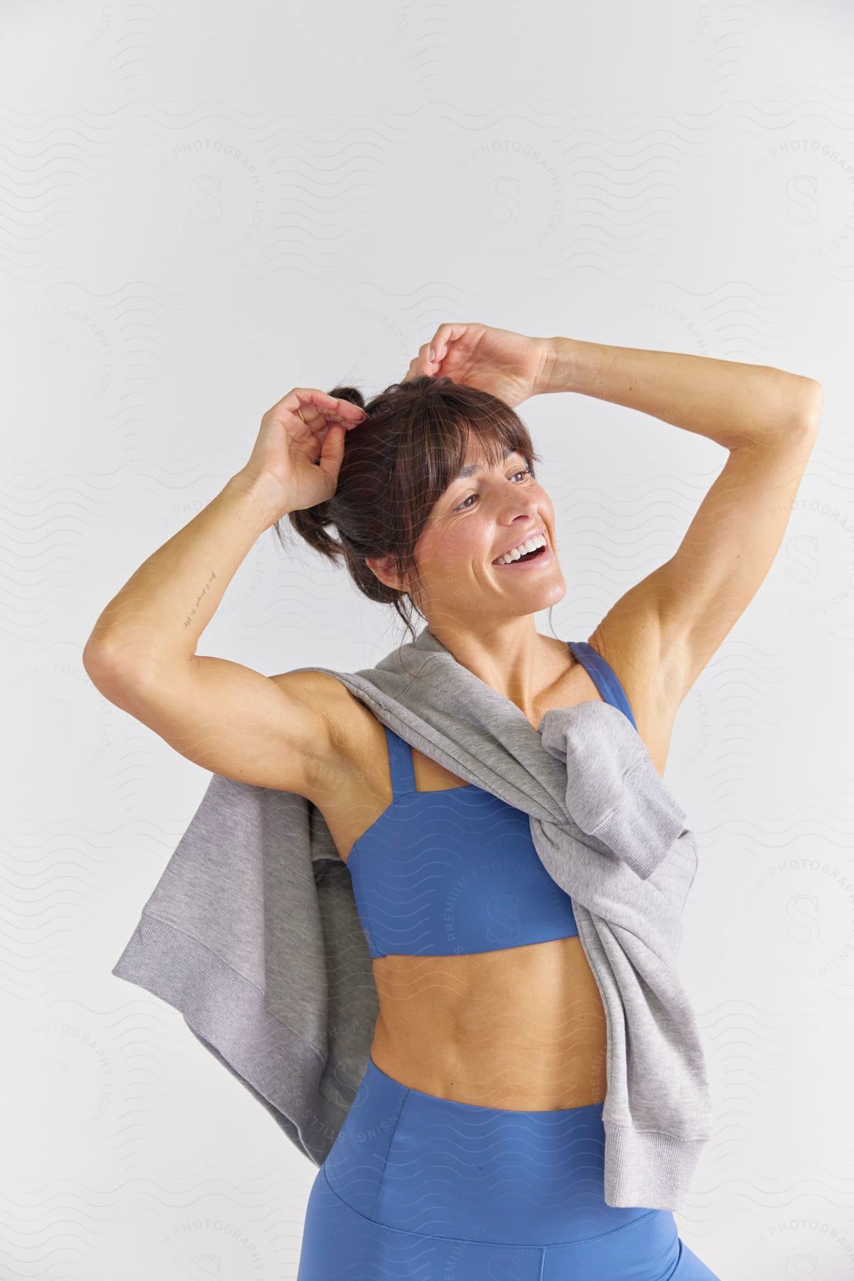 The woman is seen laughing with her hands resting on her head. She's draped in a cardigan, casually tied around her shoulders, and wearing a sleeveless top.