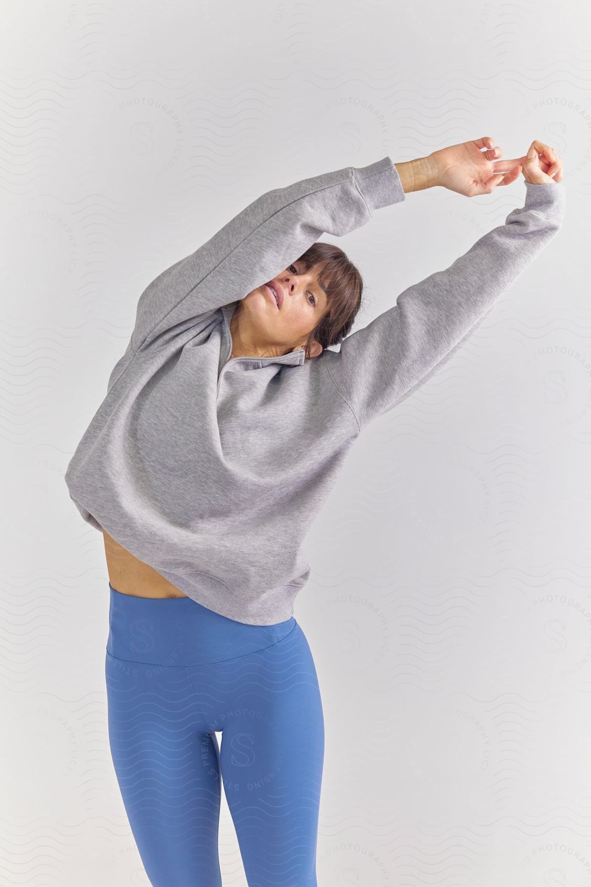 Young woman posing in a gray sweatshirt and blue leggings.