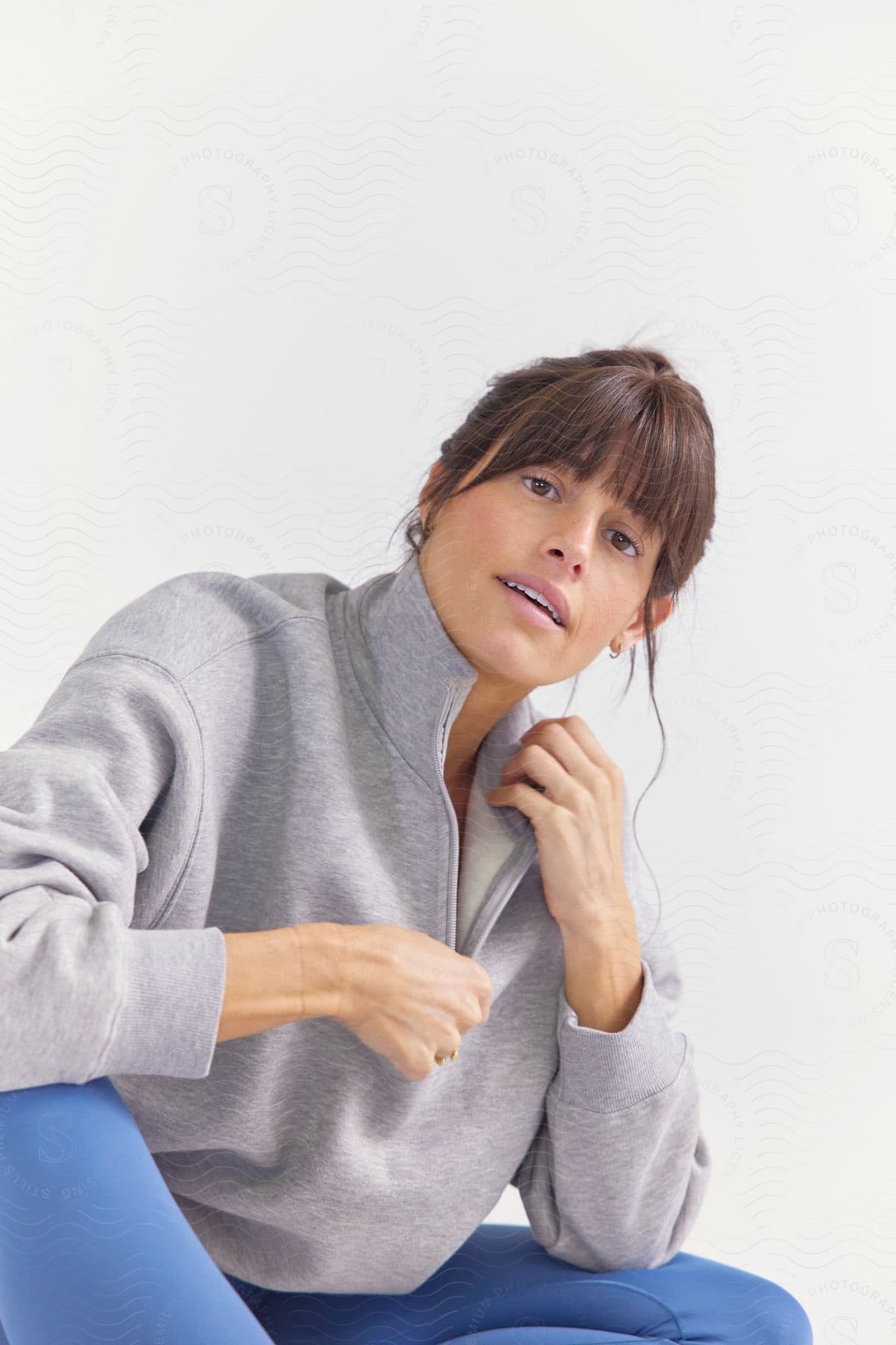 Stock photo of a woman in blue leggings, unzipping her grey sweater while making eye contact, sits on the floor.