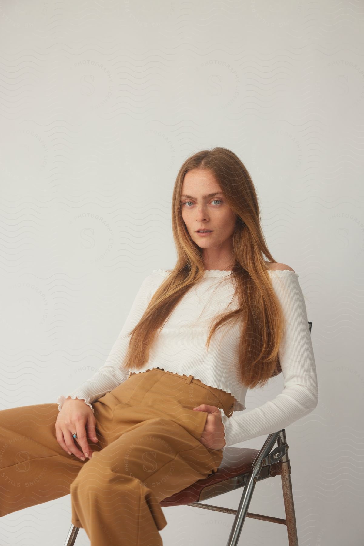 Model leans back in folding chair against a gray background.