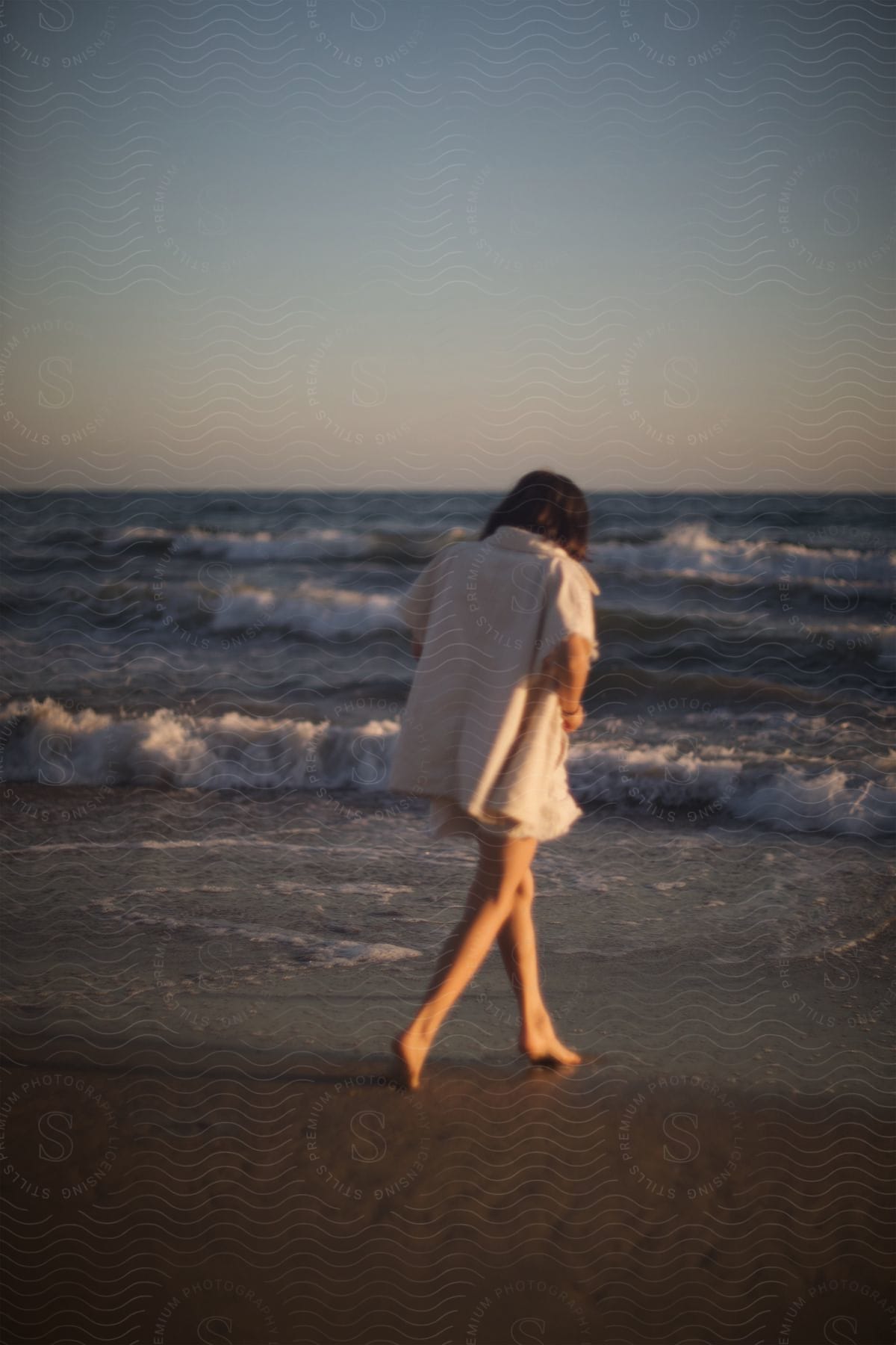 A woman wearing shorts walks along the wet sand of the beach towards the ocean waves.