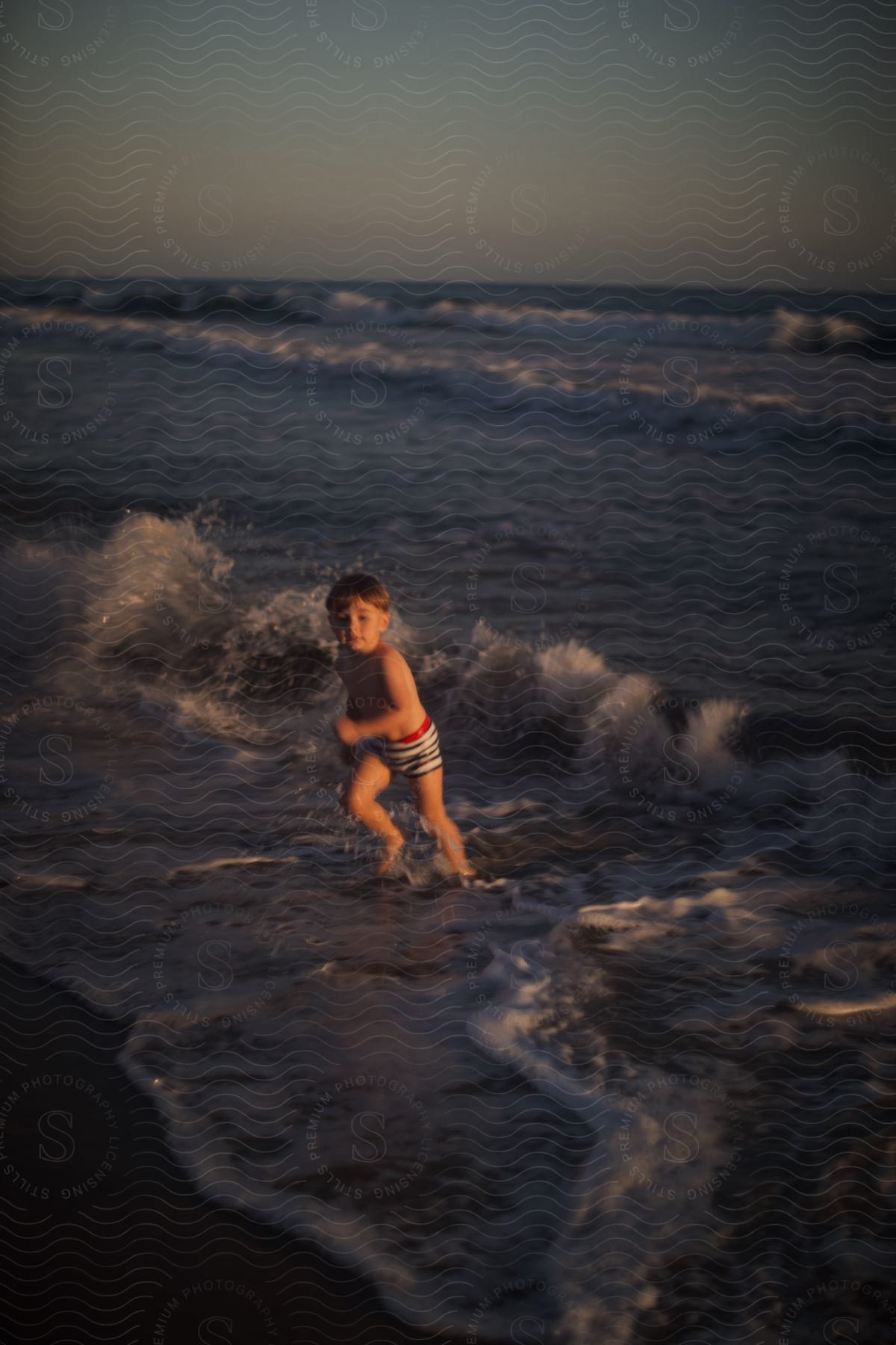 A young boy is playing on the beach in the waves.