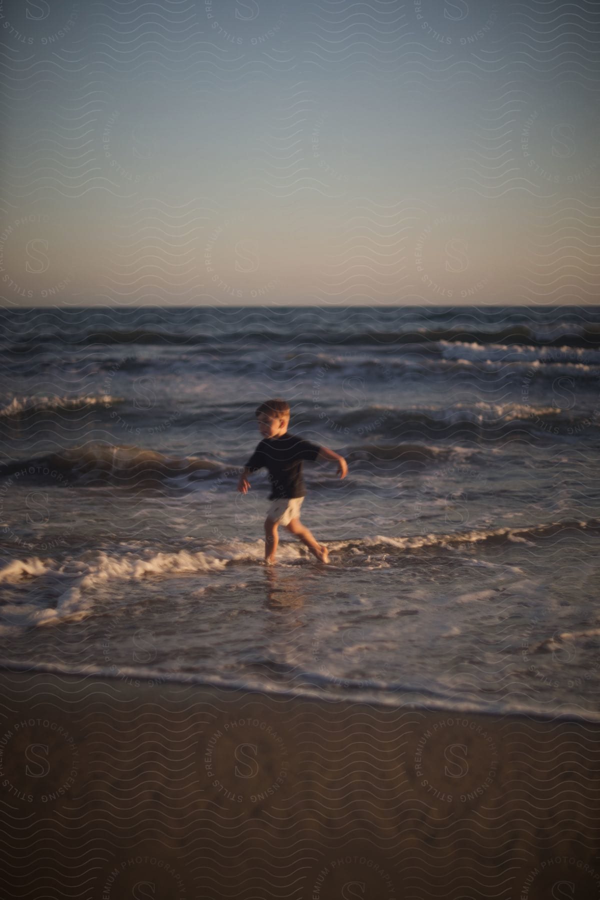 A young boy dashes onto the beach, escaping the approaching waves of the ocean at sunset.