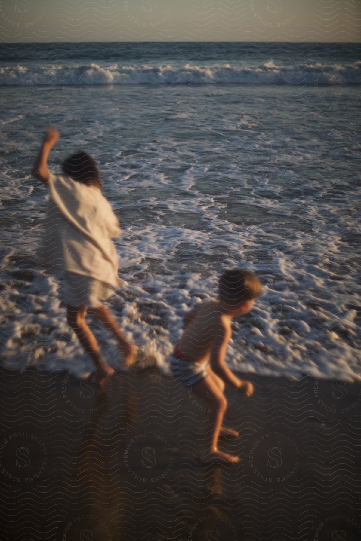 Girl and boy play together on the beach near the sea at sunset