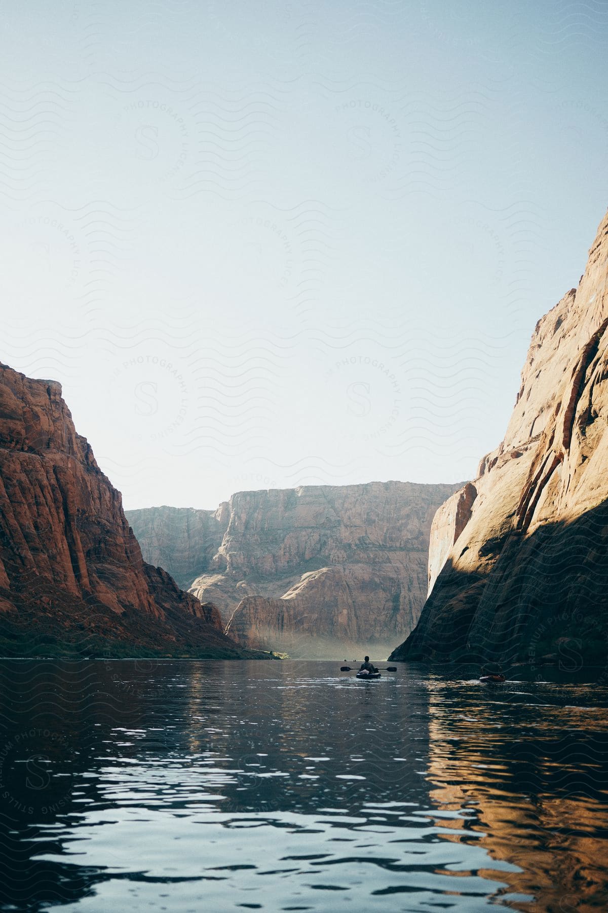 man paddling on a boat on a river next to a mountain area outdoors during day time