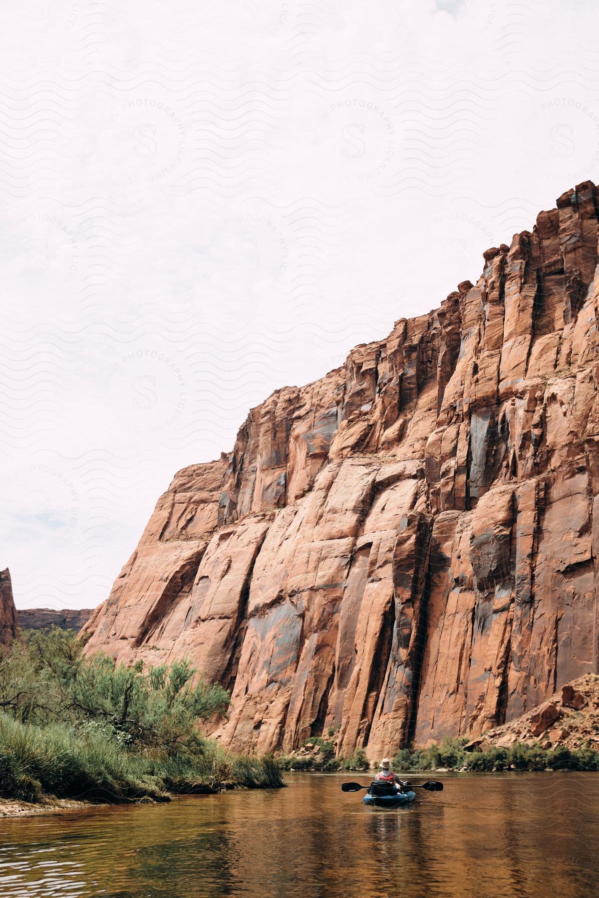 A person kayaking down a river near some cliffs.