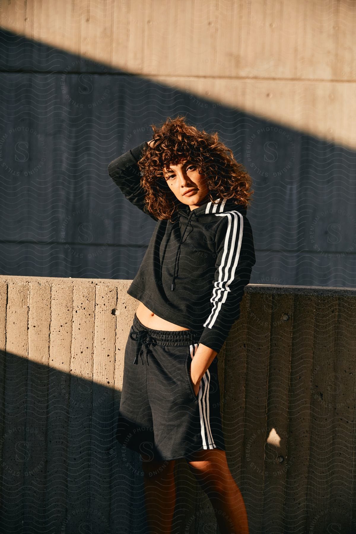 Woman with brown curly hair black hoodie and shorts poses for the camera