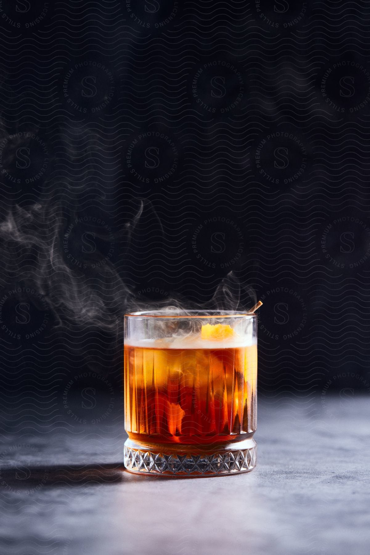 Smoke swirls around the rim of a drink in a garnished rocks glass