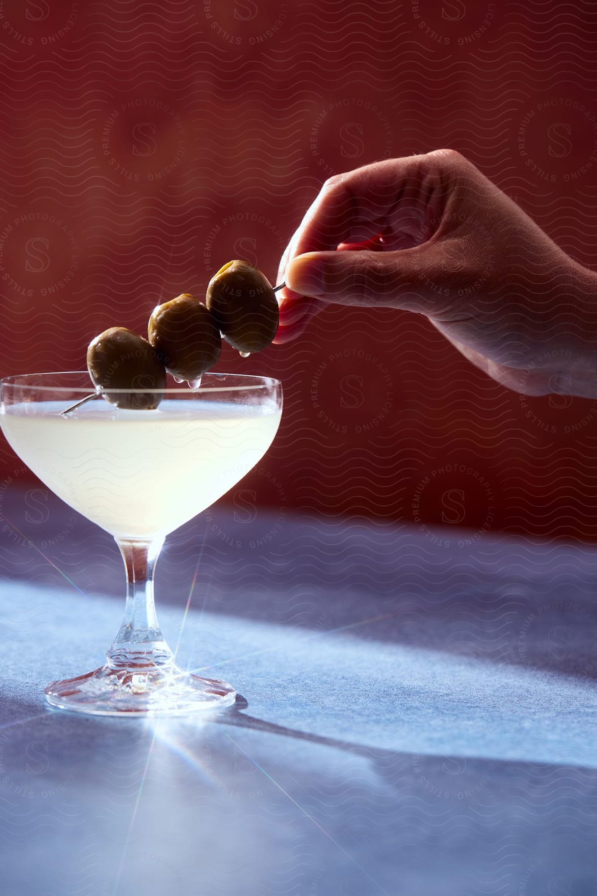 A woman is holding a toothpick with three olives in a martini glass