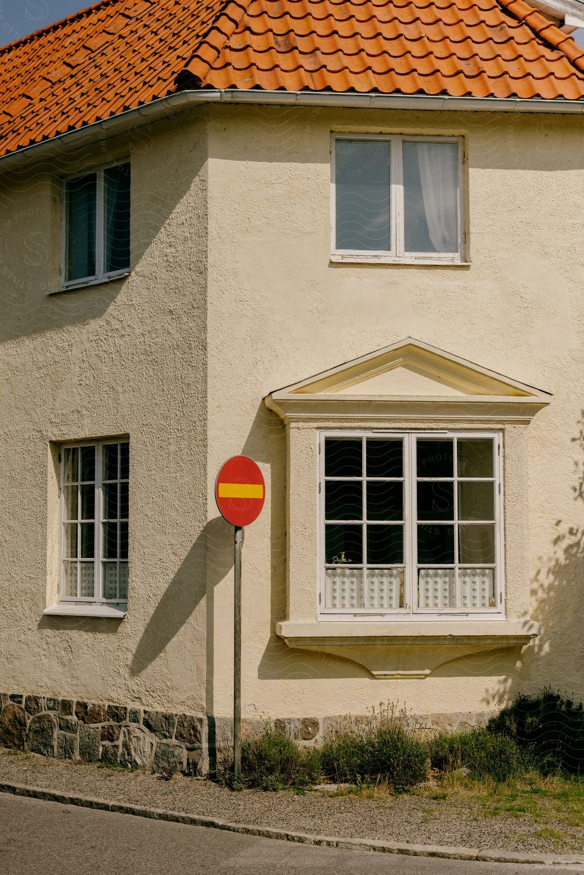 A round red sign stands next to the windows of a house close to the street of a neighborhood
