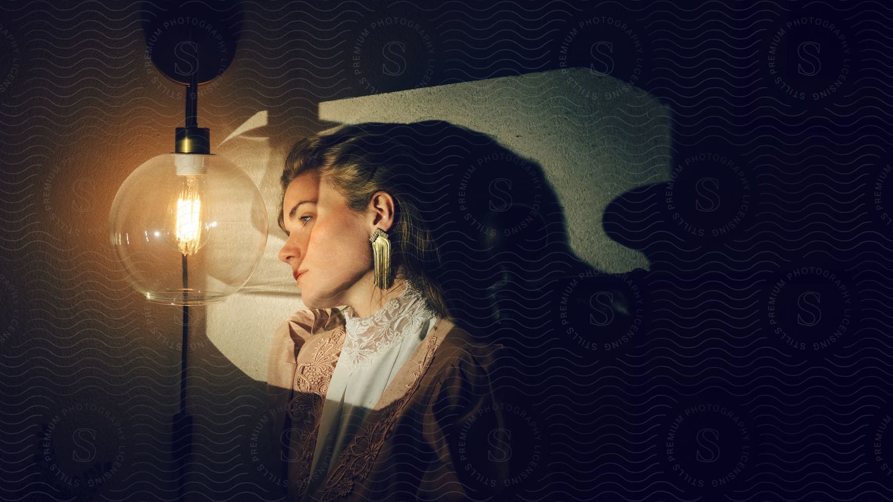 A woman stands near a wall as light from a lamp illuminates her face