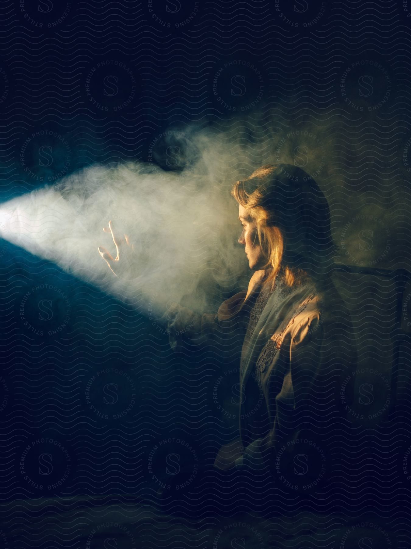A woman sitting in a dark smoke filled room reaches her hand out as light from a film projector shines upon her