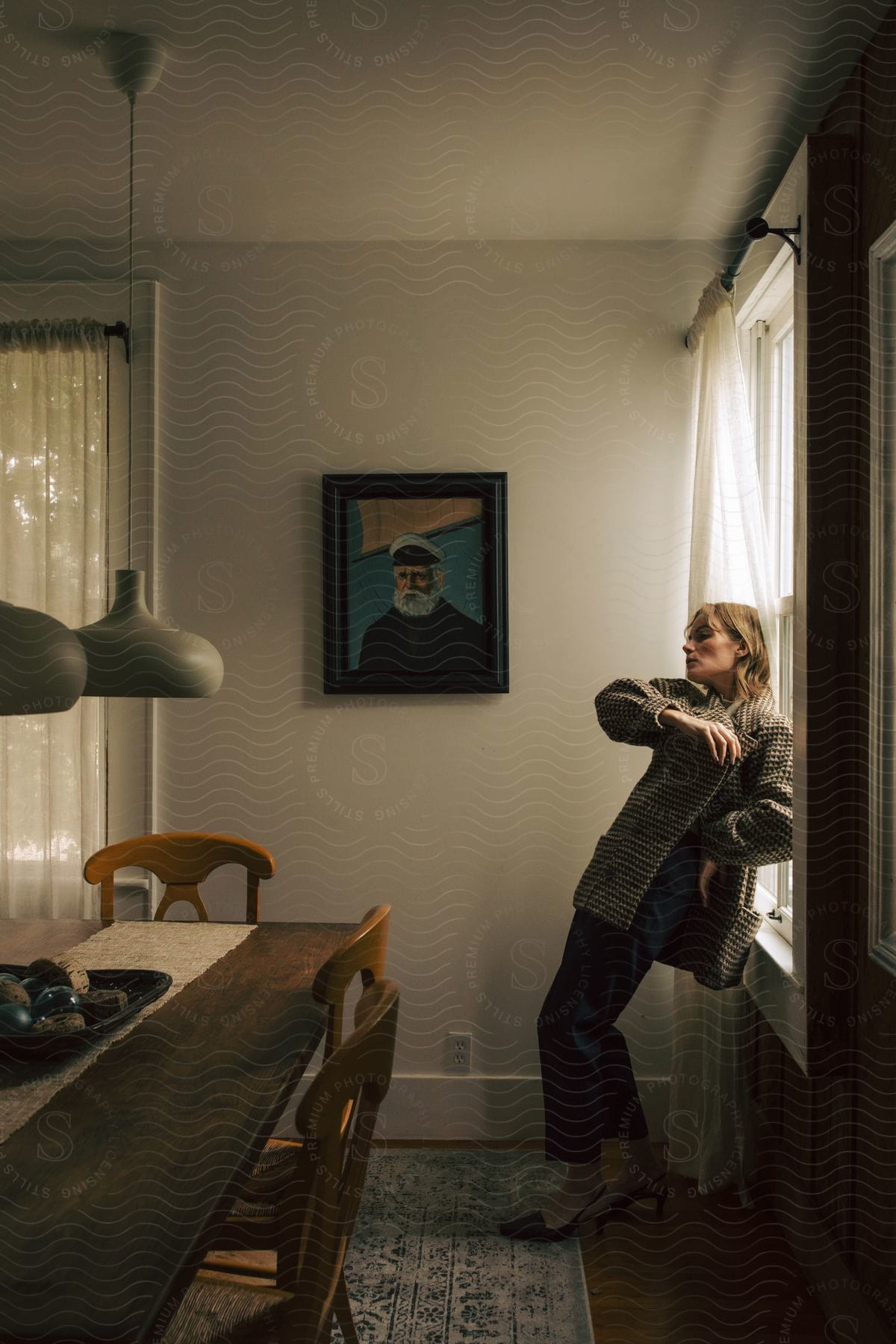 Stock photo of a woman wearing stylish clothing poses by leaning against a window in a dining room.