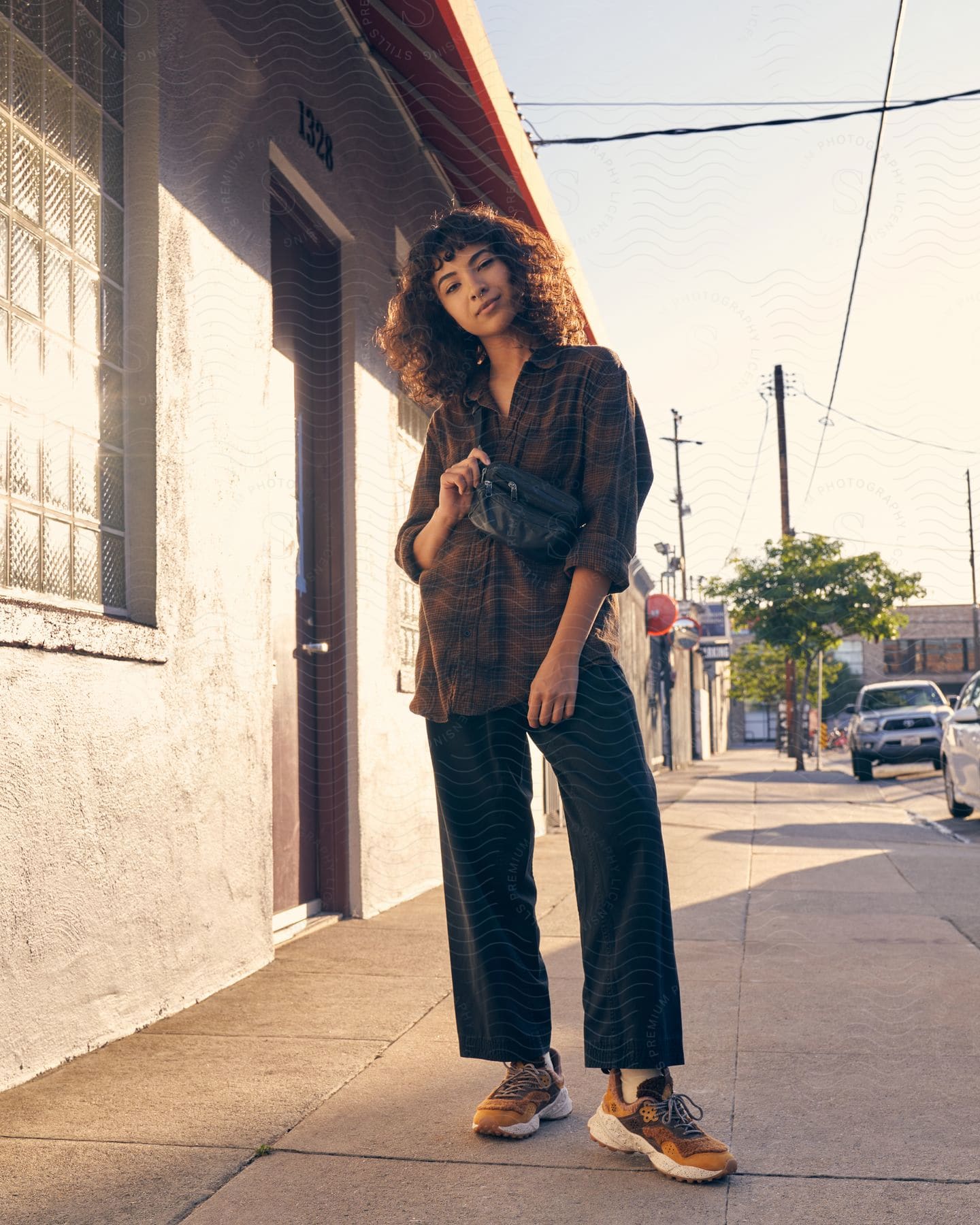 curly haired girl wearing fashion clothes standing on the sidewalk of a suburban area next to a house during day time