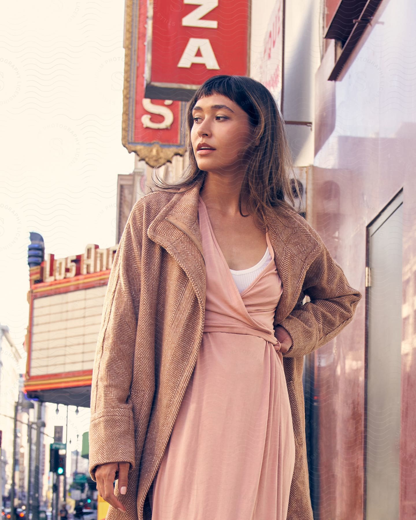 A young girl in a coat stands with one hand on her waist as she looks to her right side.