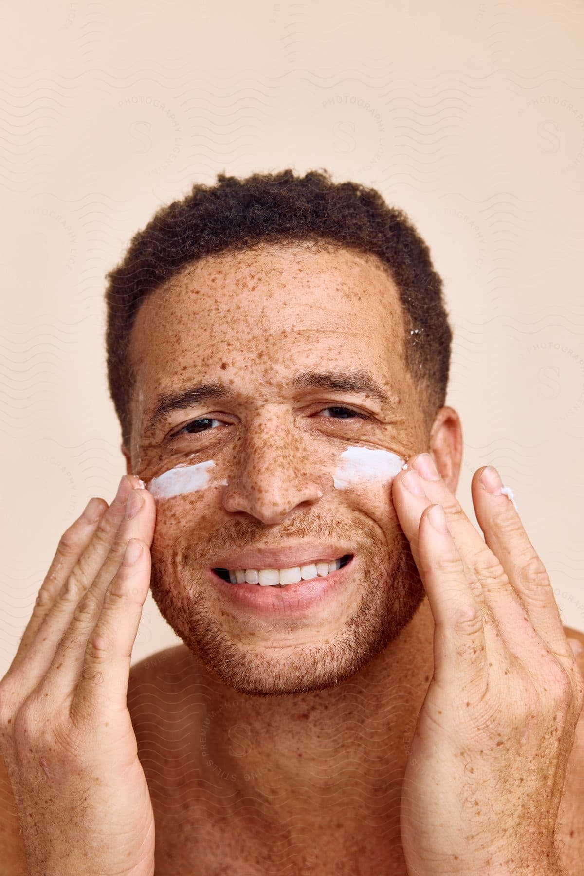 smiling man applying sunscreen cream on his face indoors