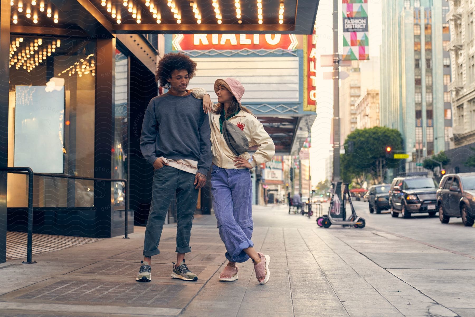 smiling young couple in fashionable clothes standing on a downtown sidewalk next to buildings and traffic during day time