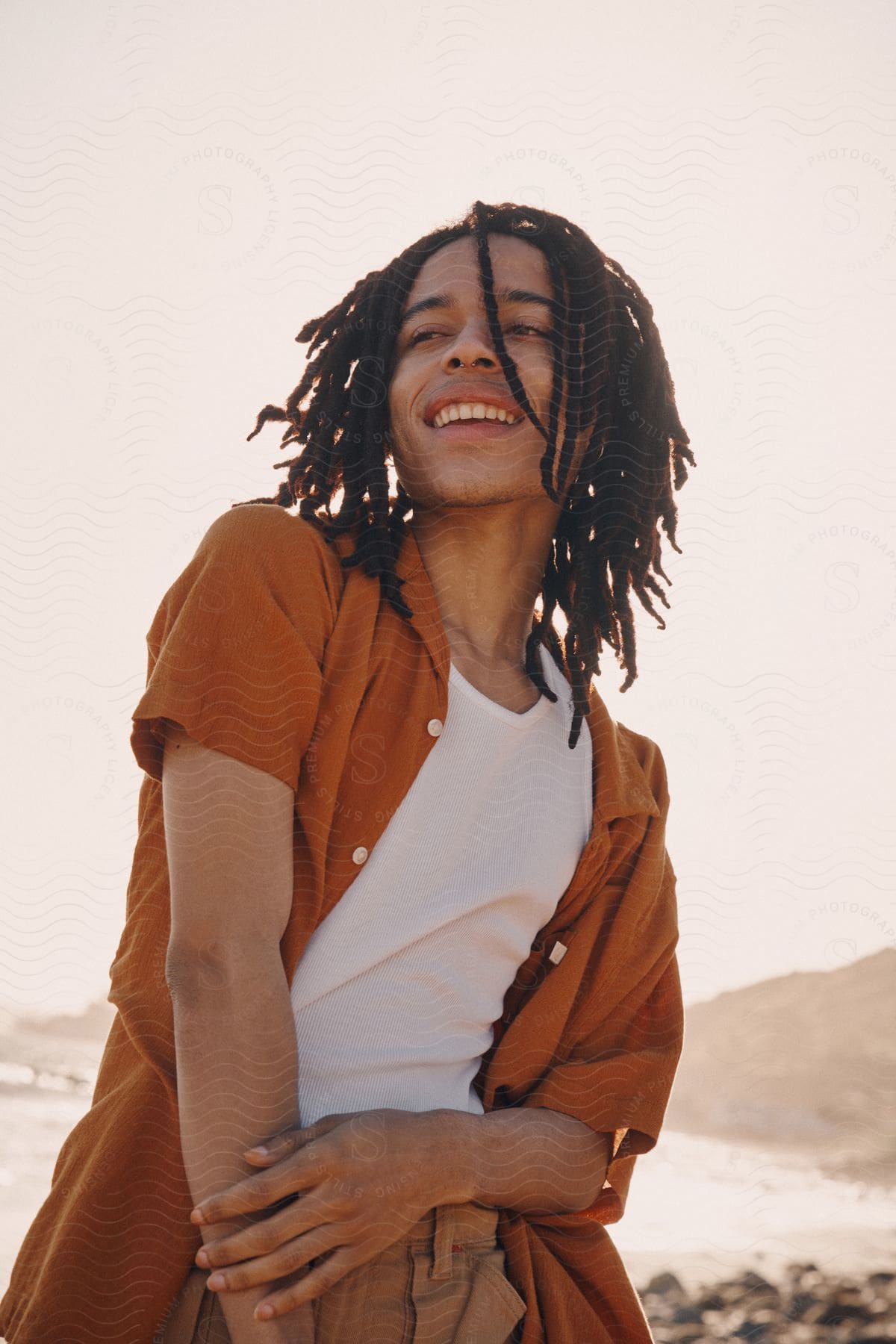 A young man smiles as he stands on the beach with his hand on his arm