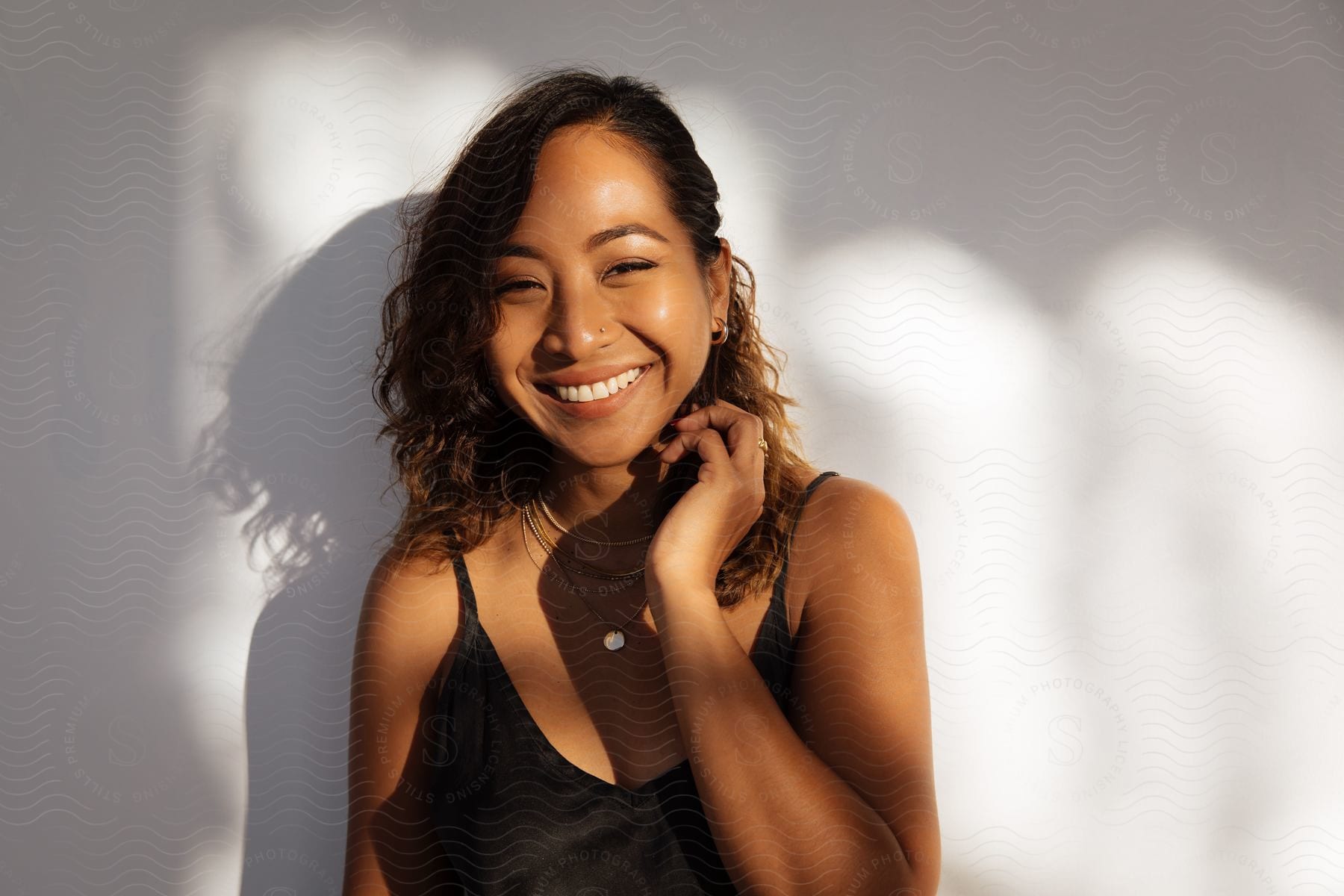 Woman with brown curly hair necklace and black Strap Top laughs at camera