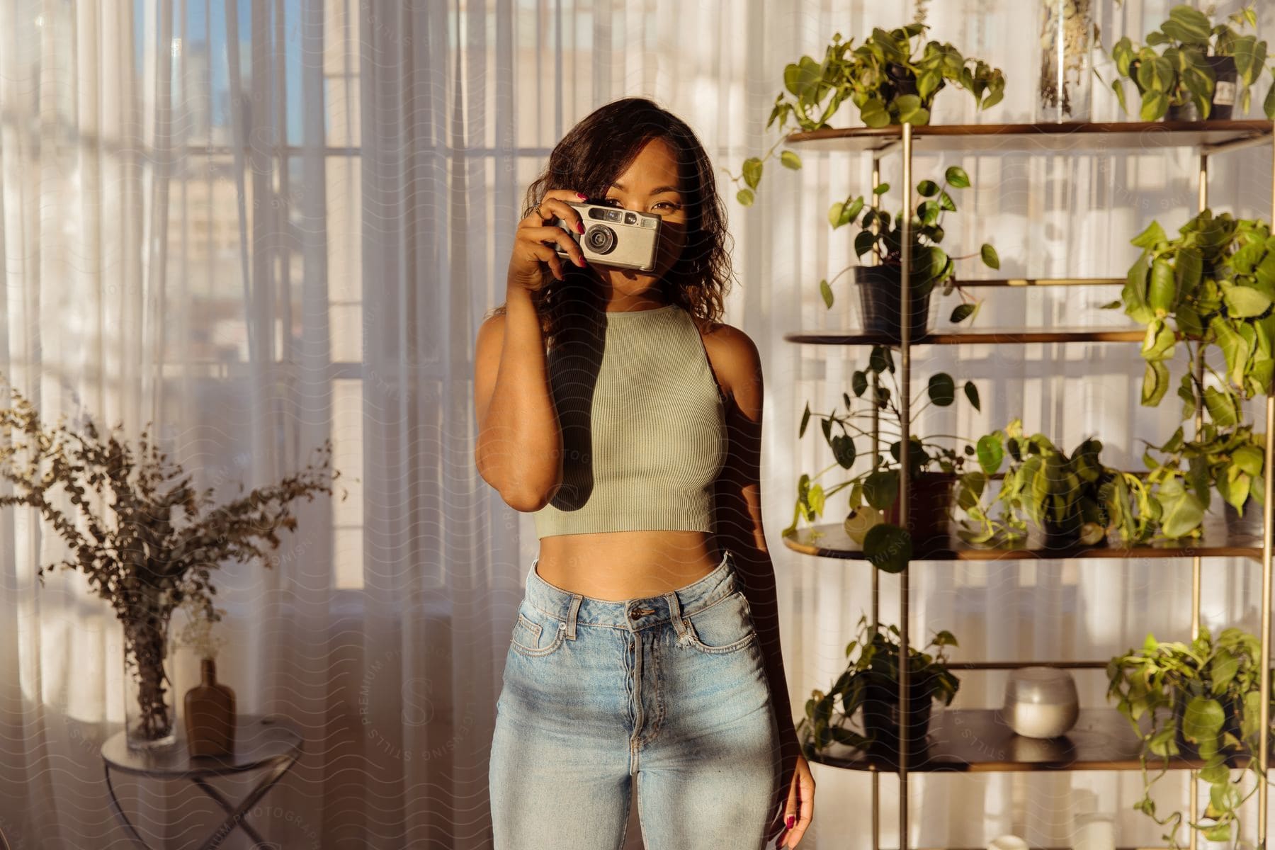 A woman is standing holding a camera to her face and her body is being illuminated by sunlight.