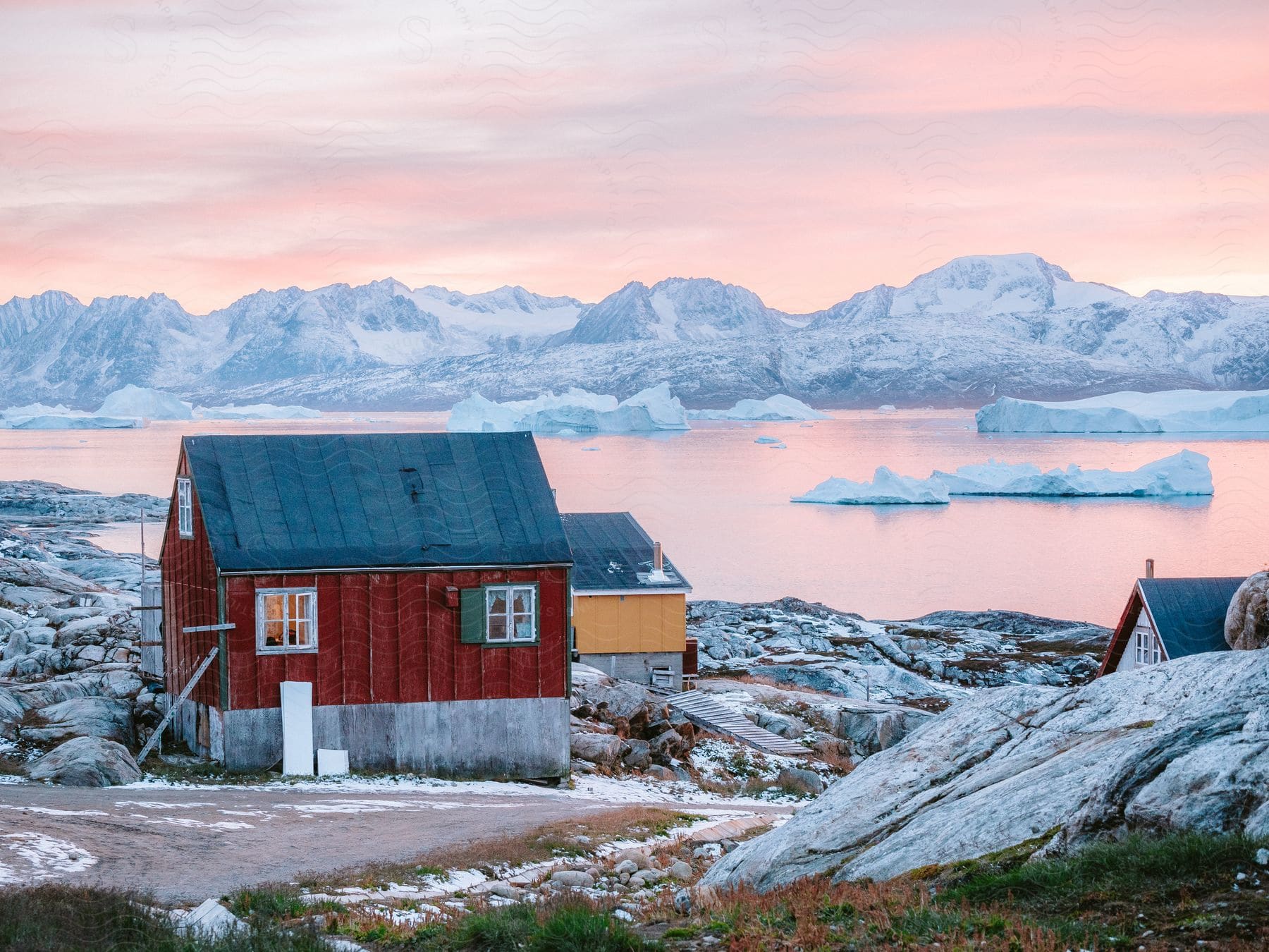 Colorful coastal homes on a rocky shore with icy water and glaciers at sun set