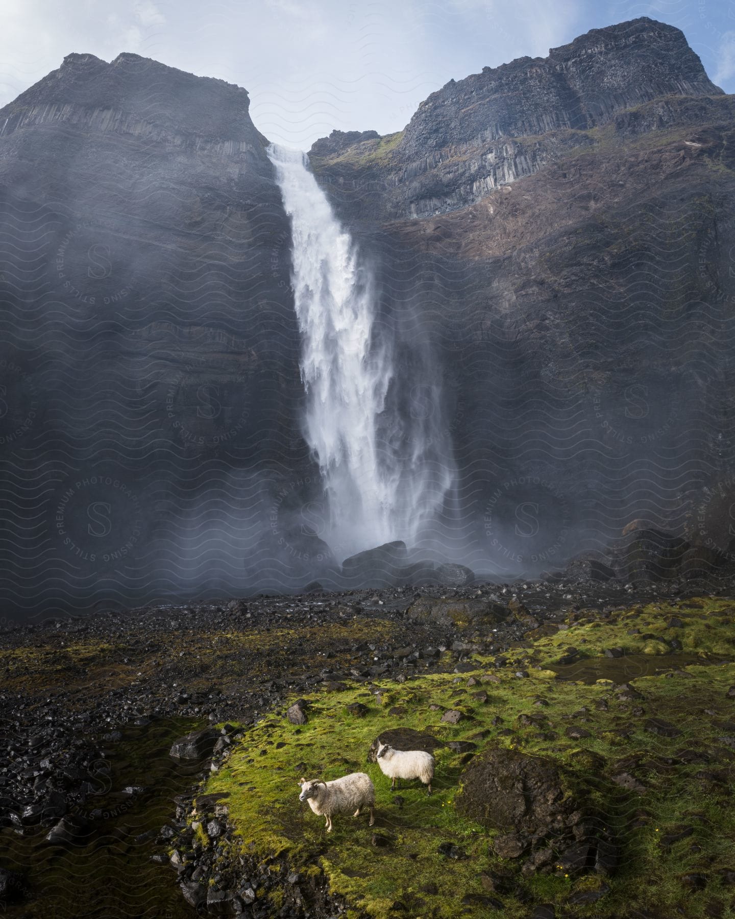 Waterfall creates mist while flowing down cliff onto rocks.