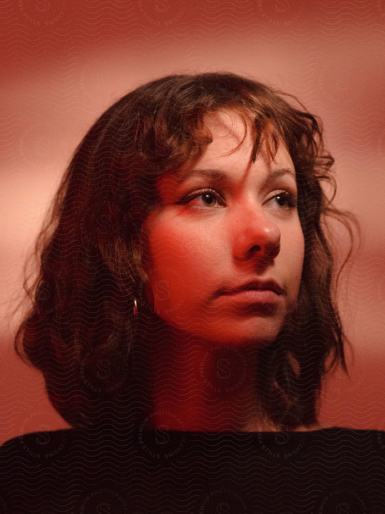 A young woman looking off to the left standing in front of a pink background