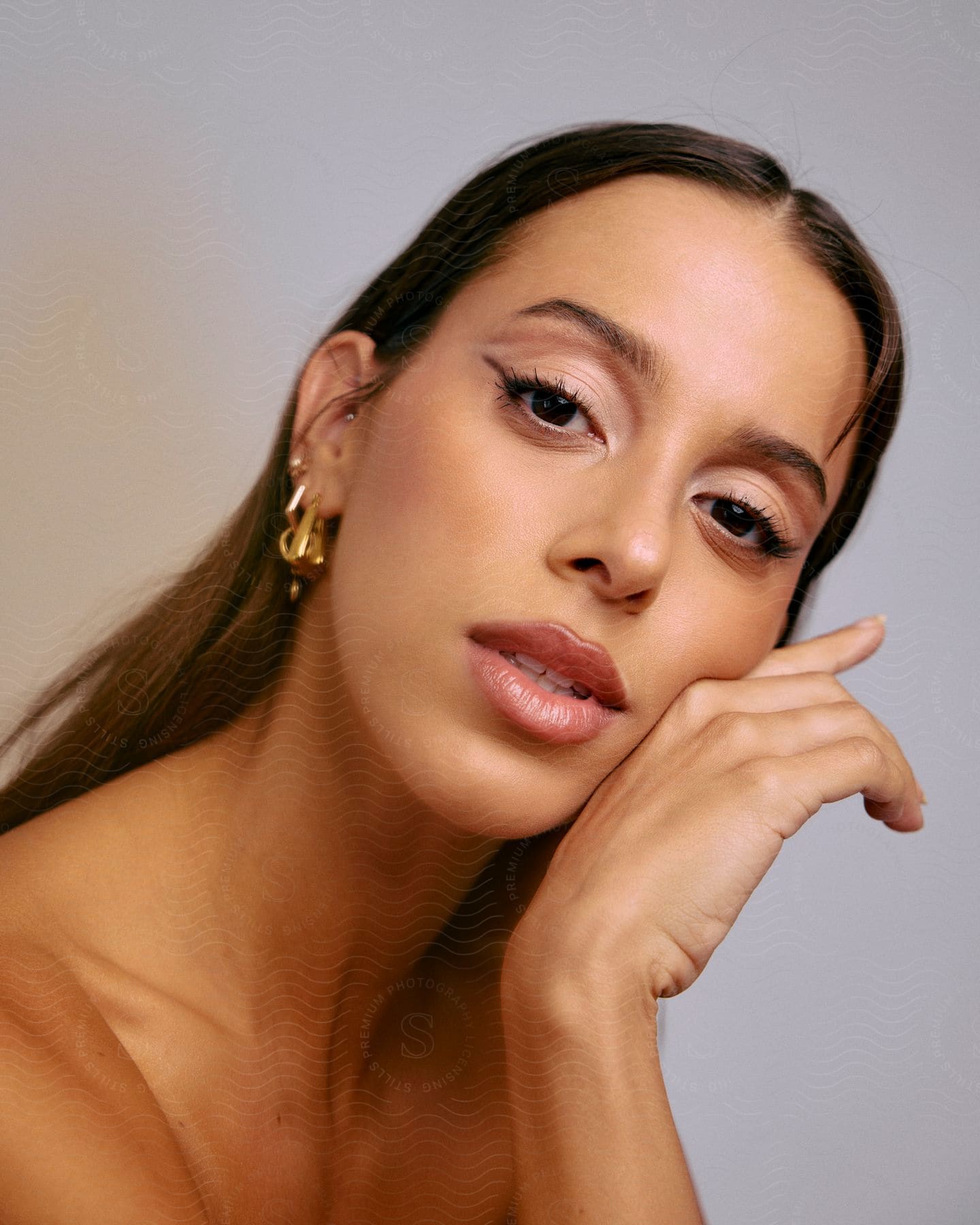 A brunette woman with red lipstick poses for a picture, her hand on her chin and a large pair of earrings framing her face.