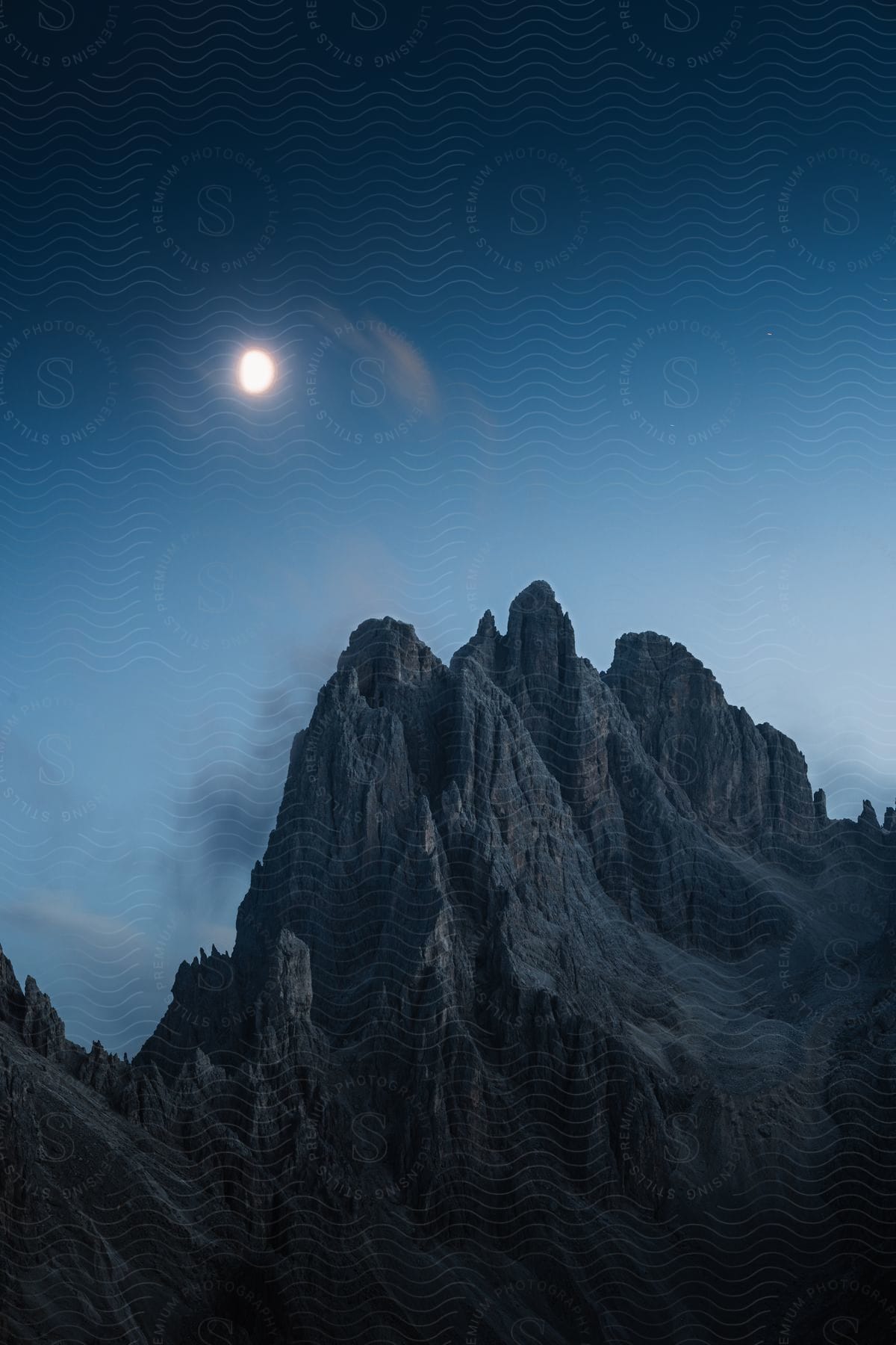 Steep rocky mountain peaks in the moonlight at dusk.