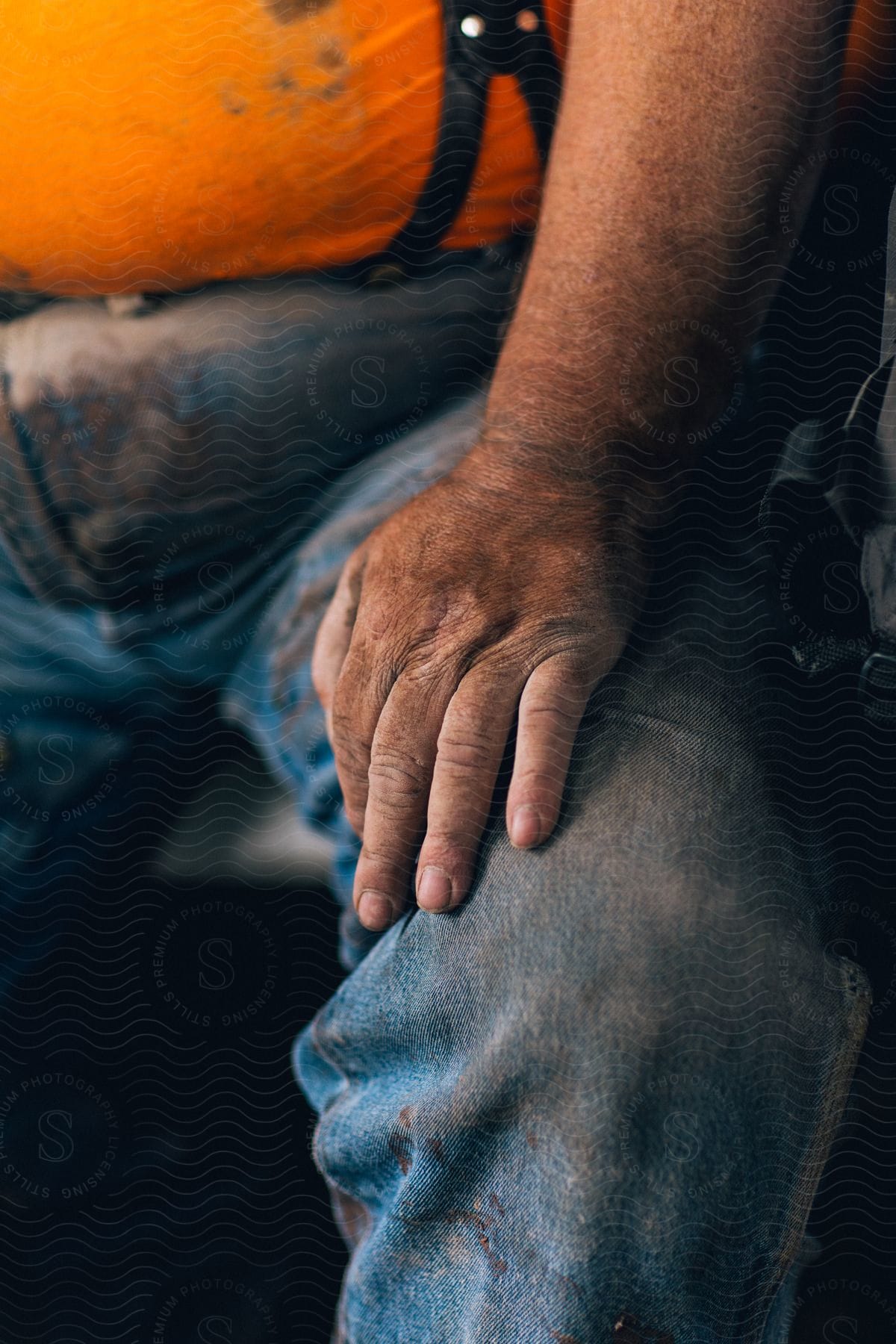 a blue collar worker rests his dirt covered hand on his thigh