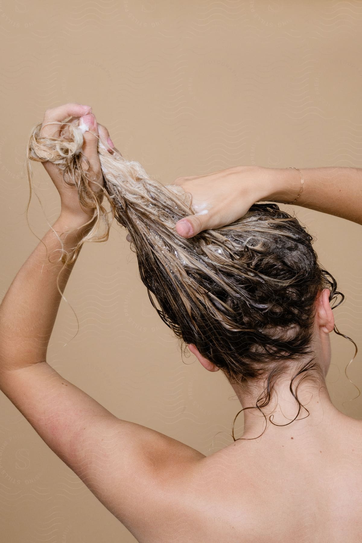 A woman with her back turned, washing her curly hair with blonde highlights.
