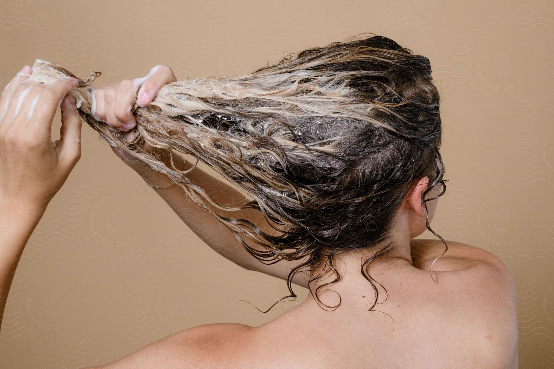 A woman with her back turned, washing her curly hair with highlights.