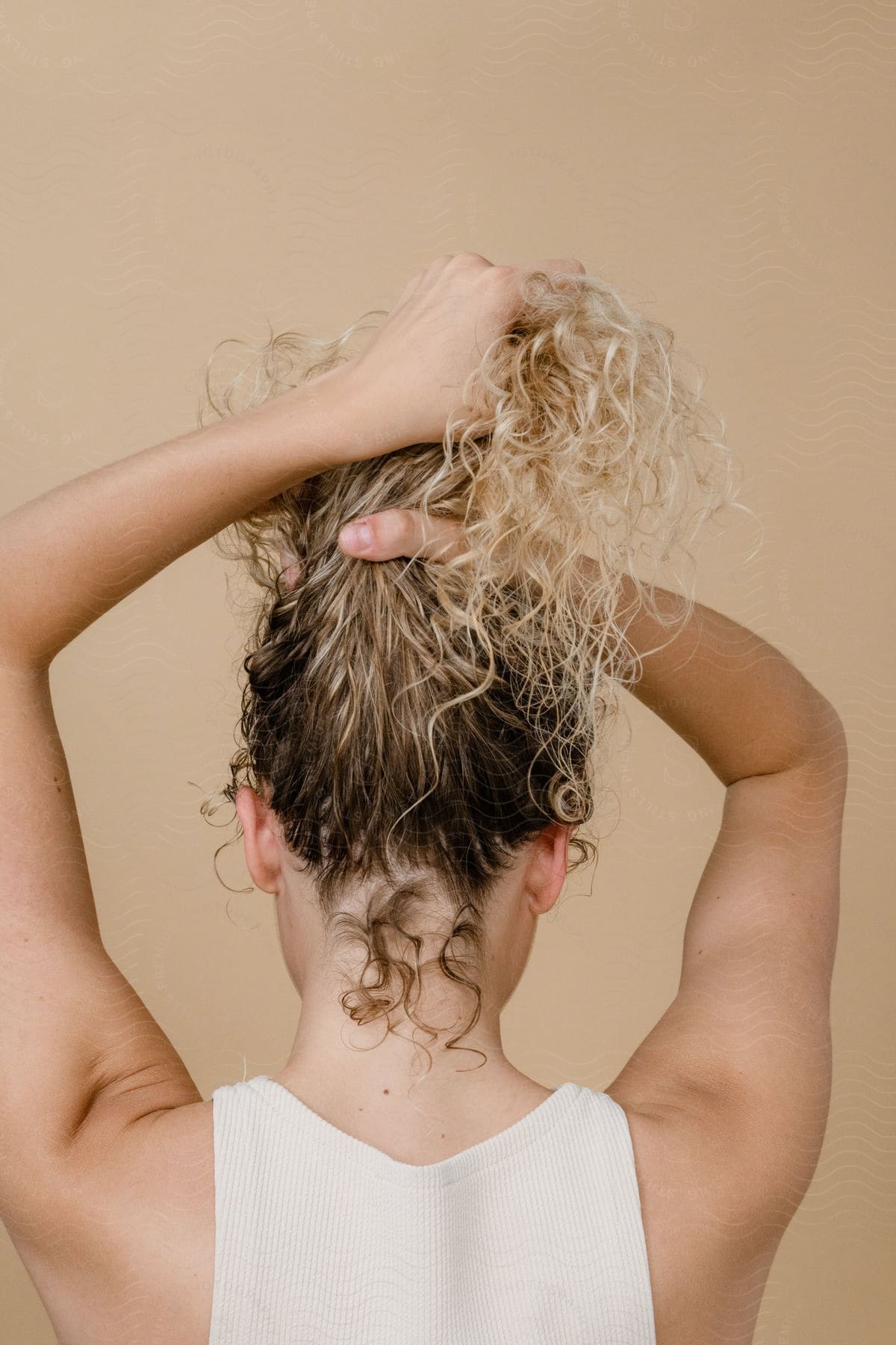 A blonde woman with curly hair, seen from behind, holding her hair.
