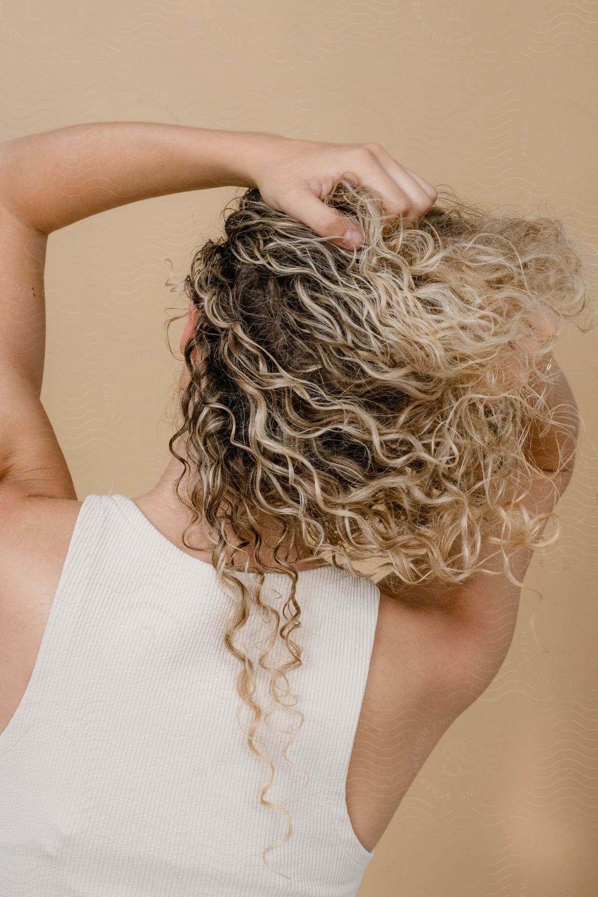 A woman with her back turned, showcasing her curly hair with blonde highlights.