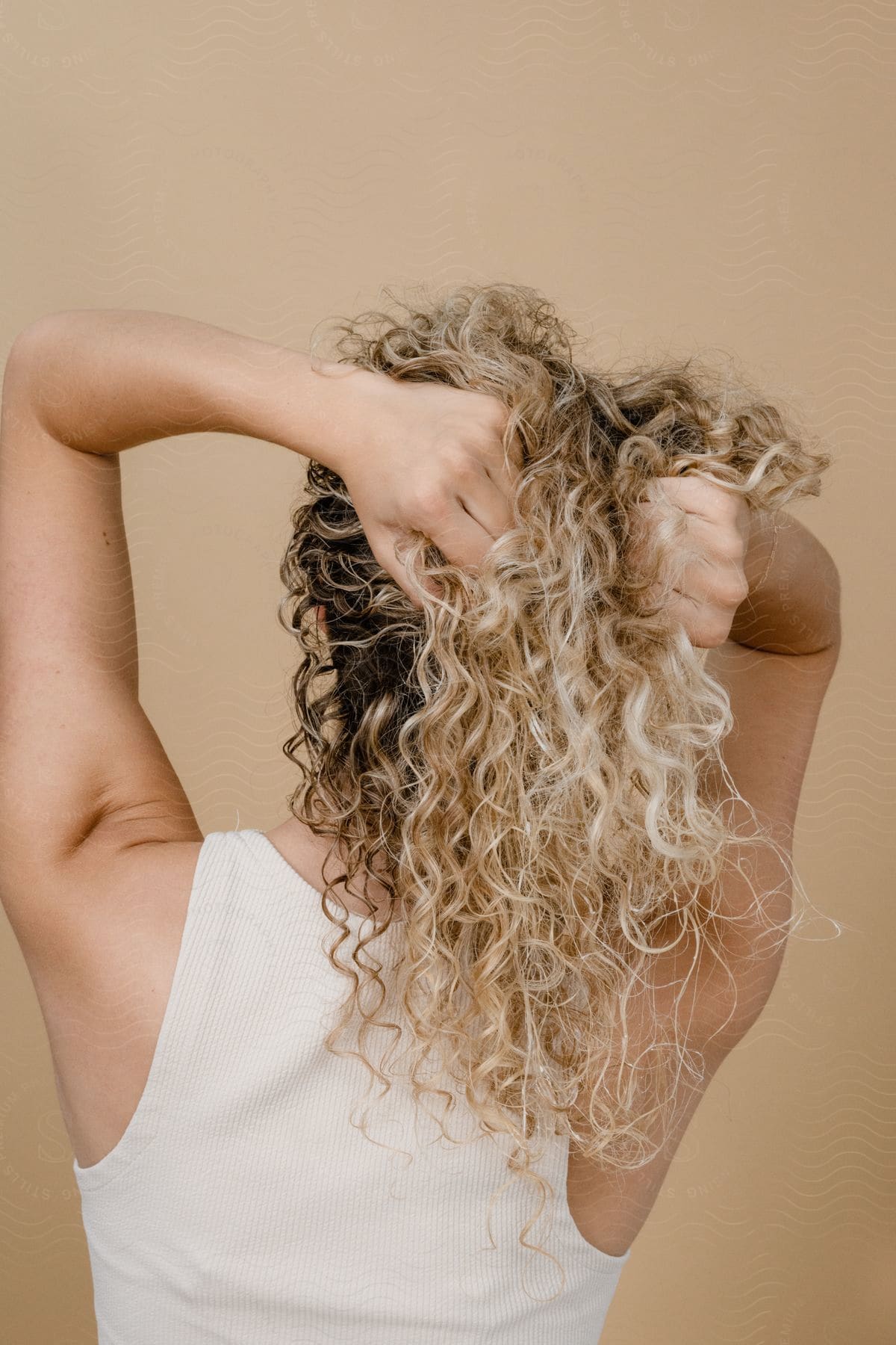 A woman with her back turned, holding her curly hair with highlights.