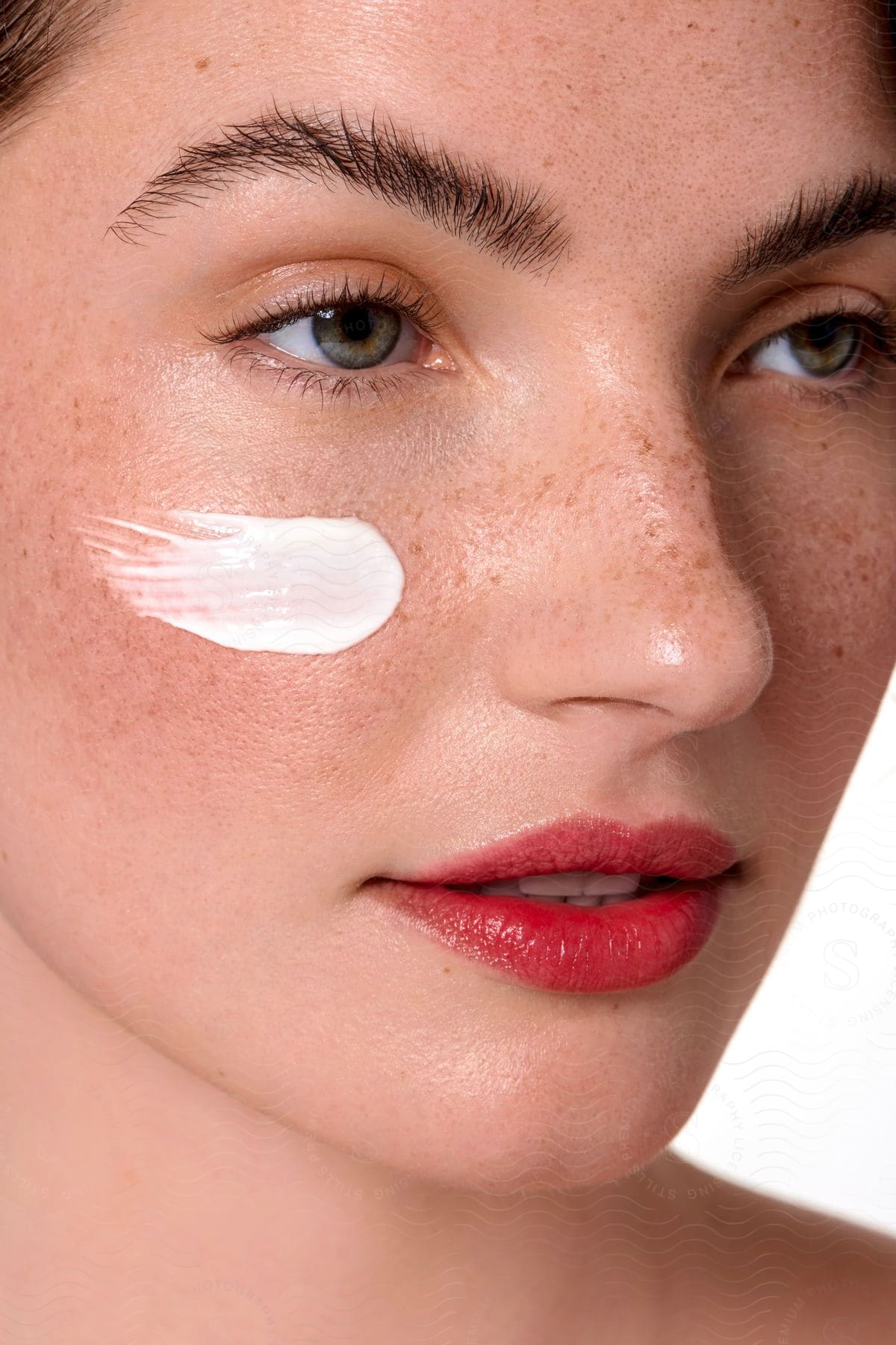 Close up of a woman with a dab of white cream on her cheek as she looks ahead